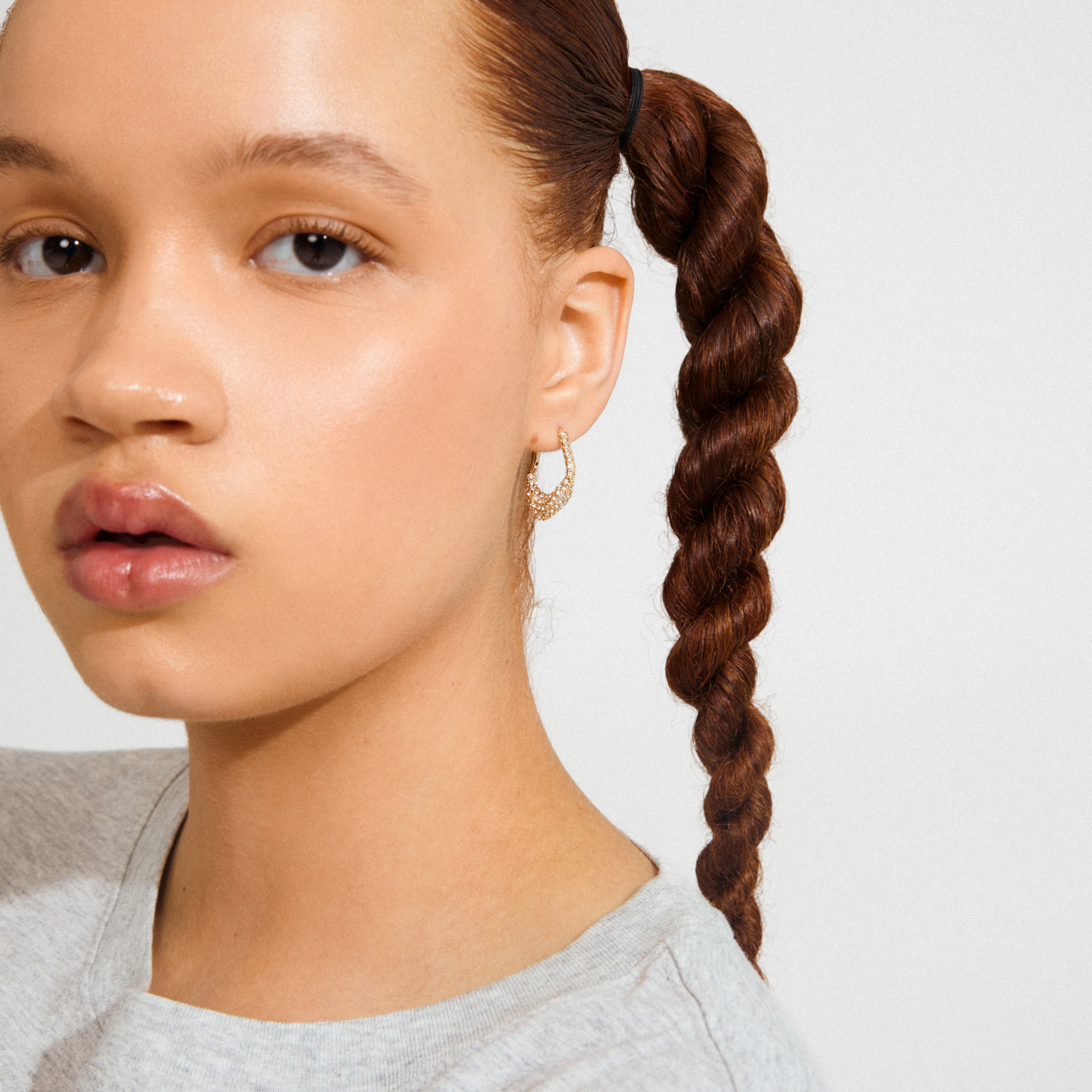 Young woman wearing Pilgrim's FENIX earrings: a gold-plated hoop encrusted with sparkling stones, showcasing a blend of elegance and dynamic style.
