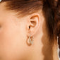 Close-up of a woman's ear wearing a gold-plated FENIX hoop earring adorned with sparkling stones, showcasing its elegant teardrop shape and dynamic design.