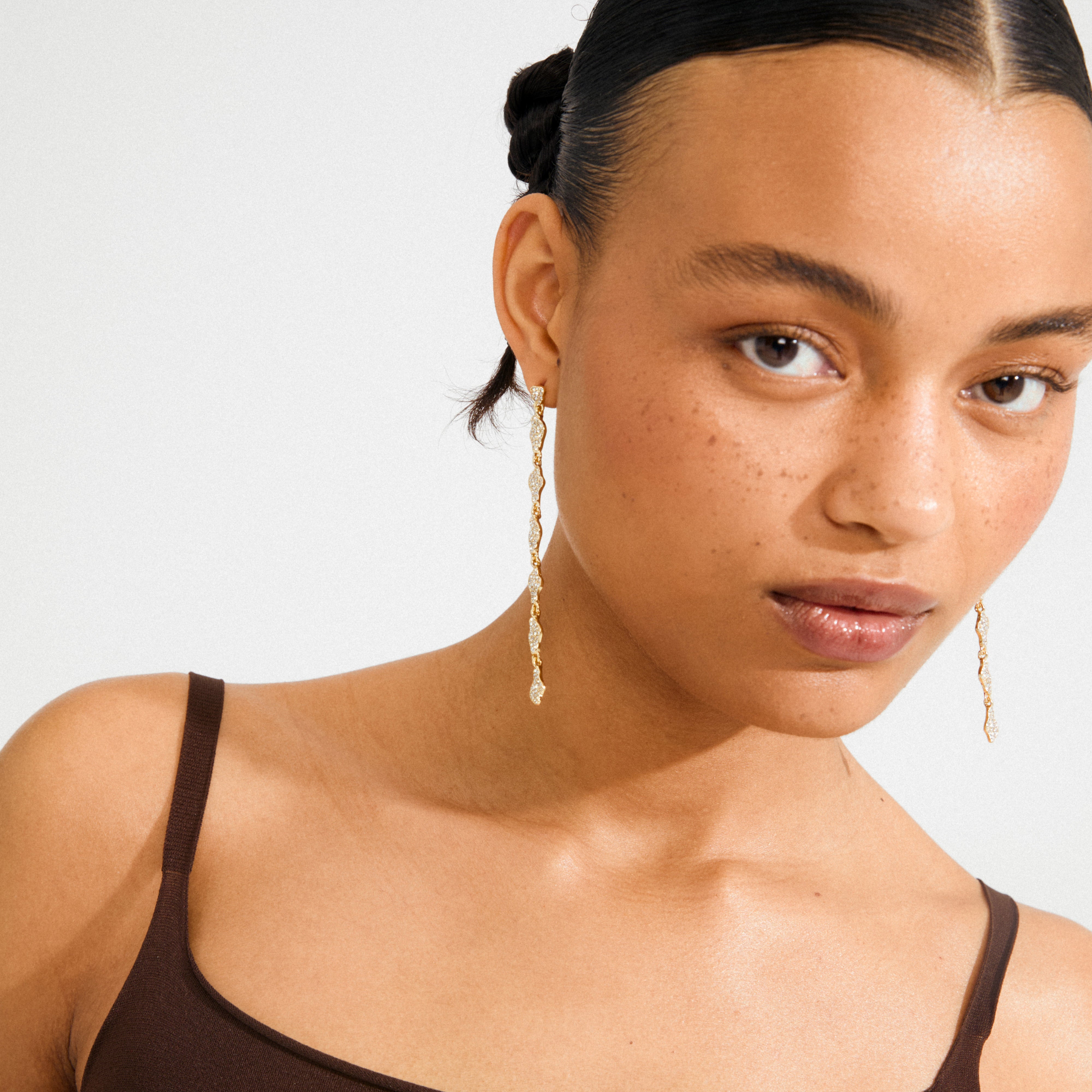 Young woman wearing Pilgrim's BASIL gold-plated drop earrings adorned with Preciosa crystals, showcasing a luxurious and dynamic silhouette for an effortlessly sophisticated look.