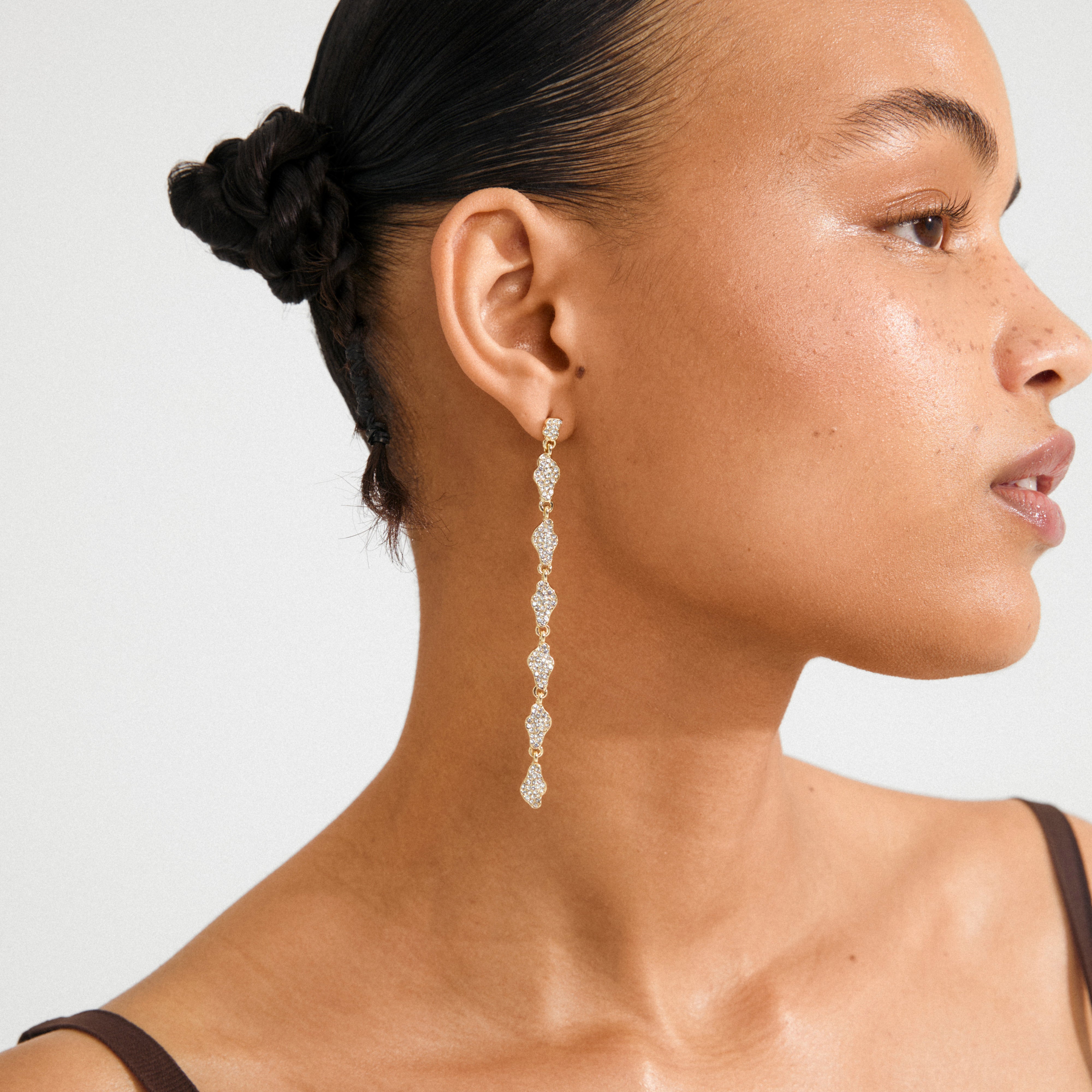 Woman wearing BASIL earrings gold-plated by Pilgrim, featuring linked, diamond-like shapes with Preciosa crystals, showcasing a chic, sophisticated look.