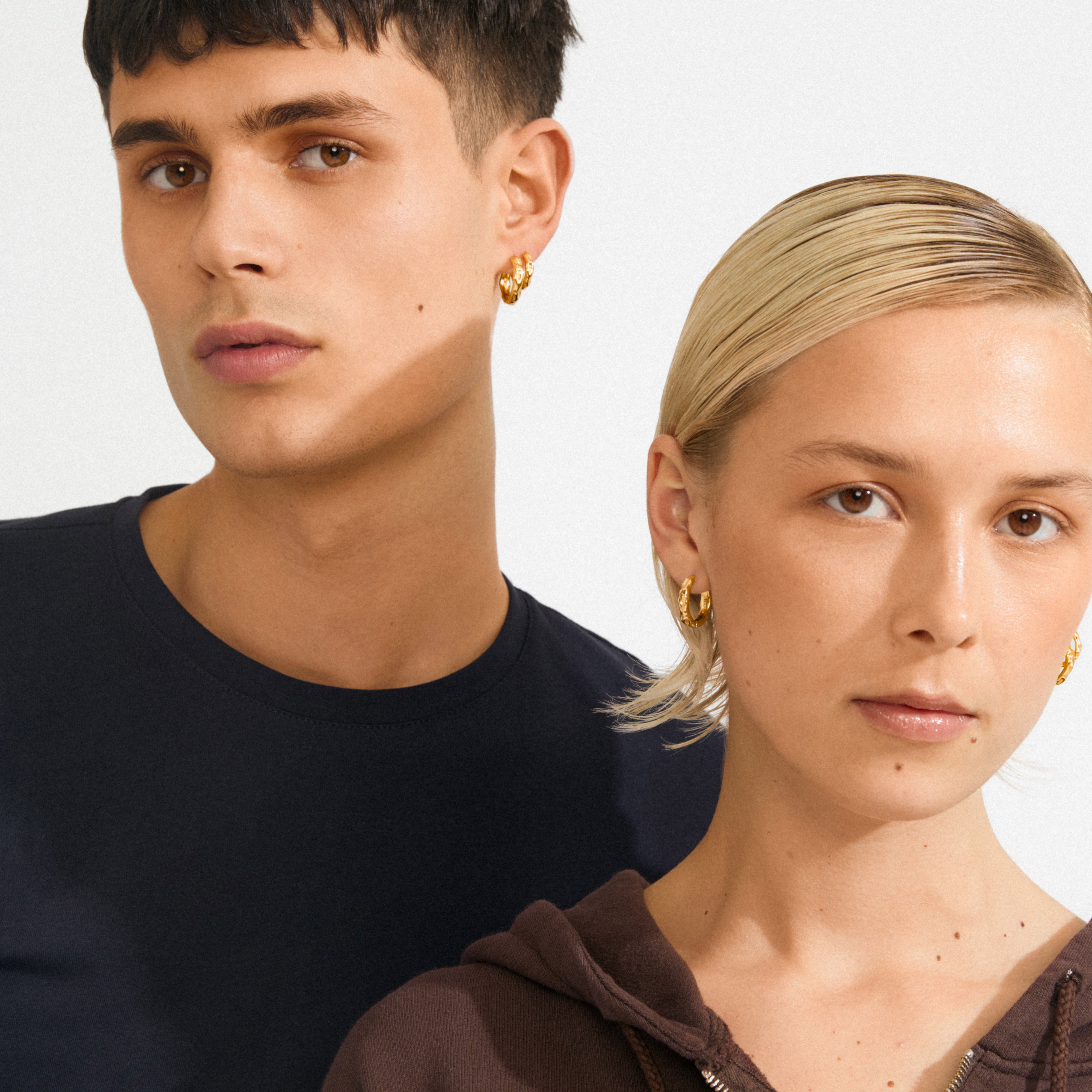 Two young adults wear the gold-plated DARBY earrings, 2-in-1 set, showcasing the classic hoops' wavy design, perfect for minimalist and stacked styles.