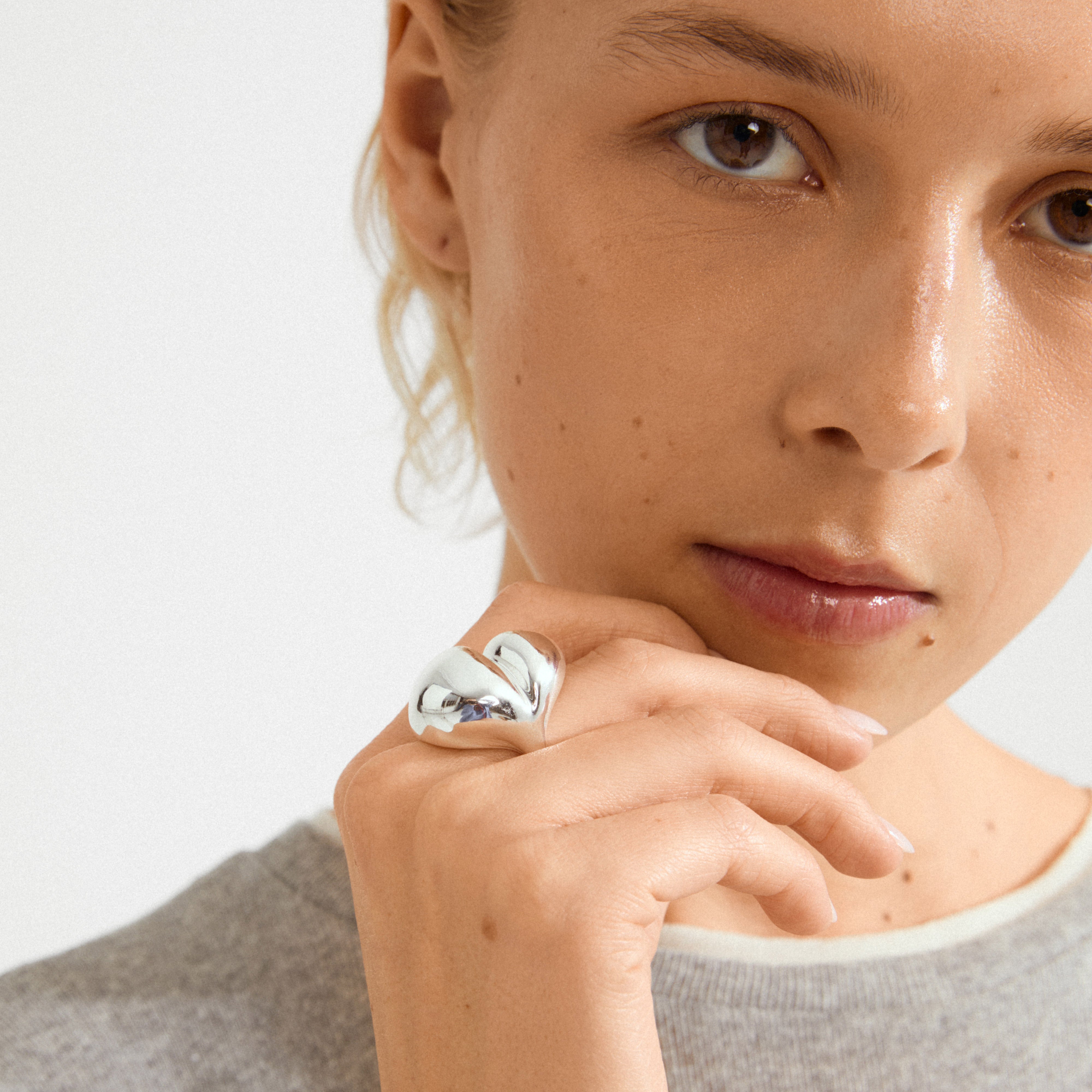 Person's hand with MADDIX silver-plated ring, showcasing its bold, sculptural wave design. The ring's shiny surface stands out against the minimalist style.