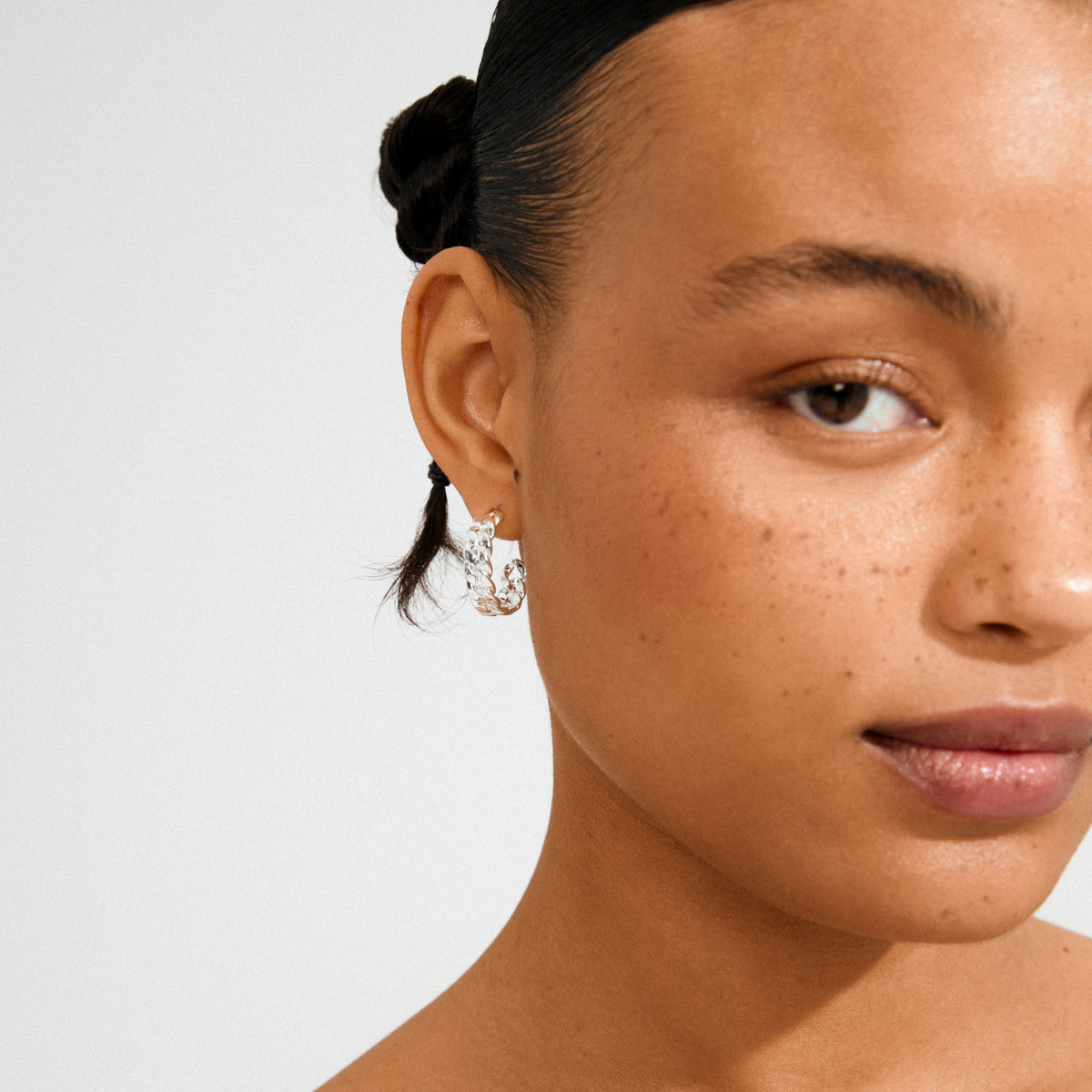 Young woman wearing Pilgrim's MAYER silver-plated chunky hoop earrings, showcasing their iconic curb chain design against her smooth, freckled skin and braided hairstyle.
