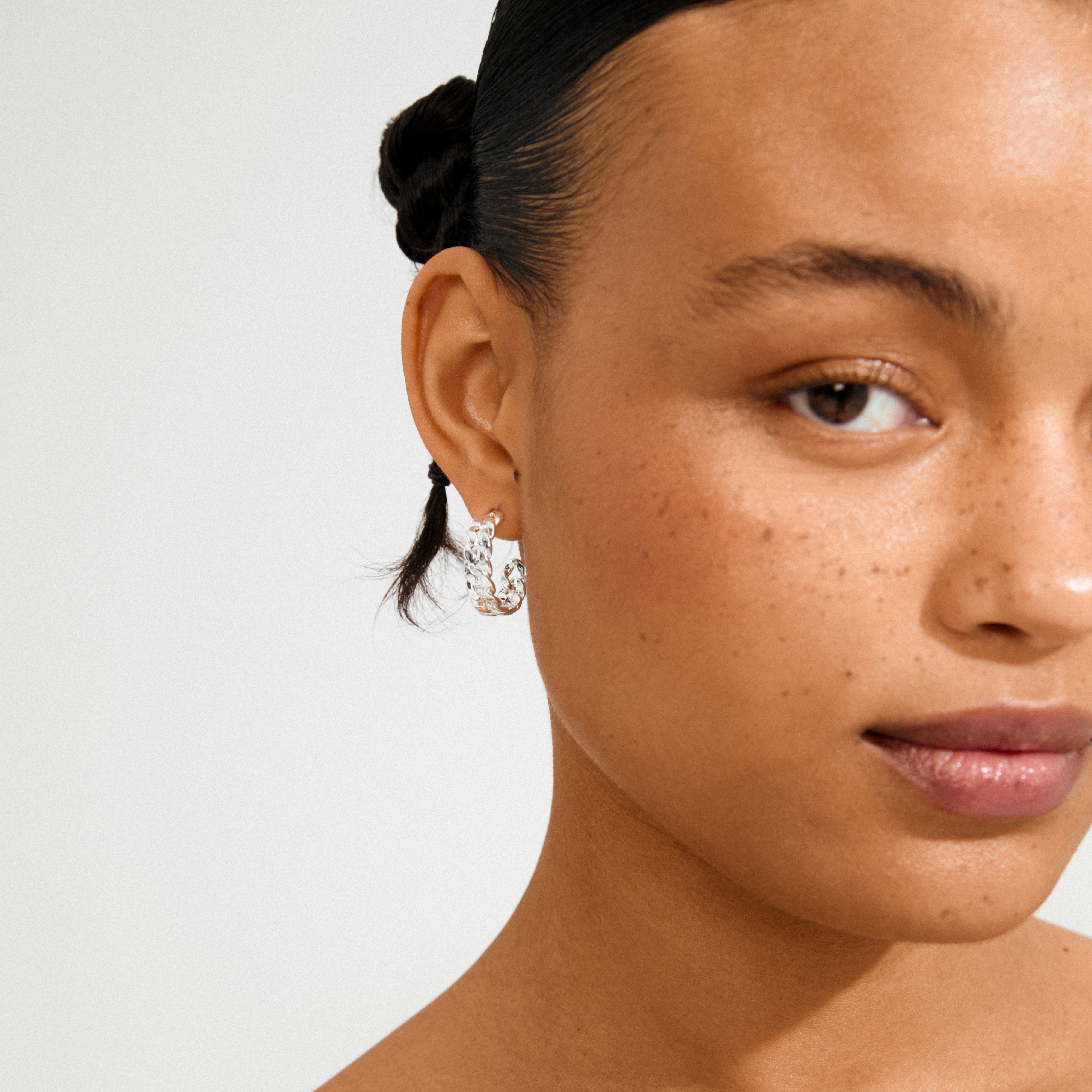 Young woman wearing Pilgrim's MAYER silver-plated chunky hoop earrings, showcasing their iconic curb chain design against her smooth, freckled skin and braided hairstyle.