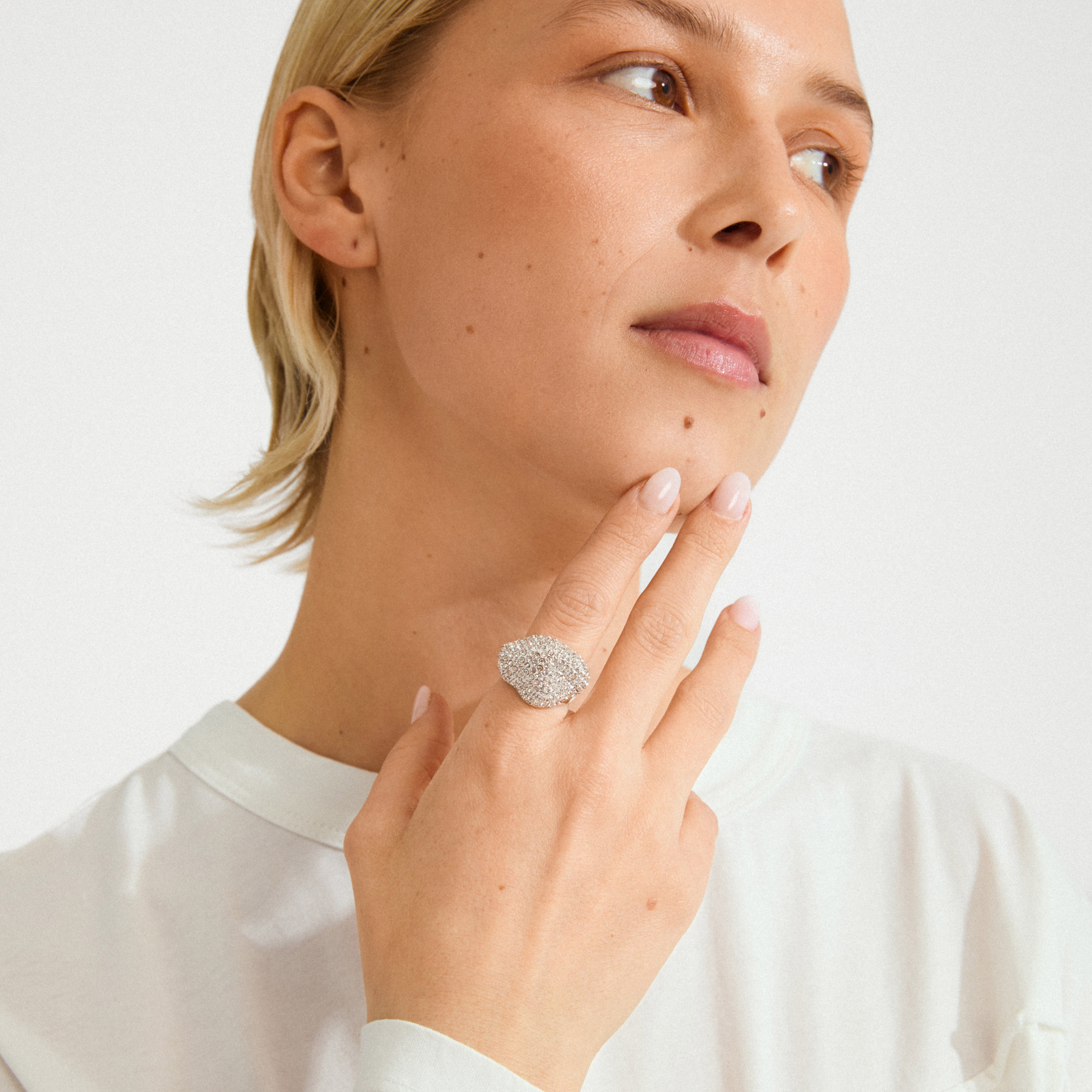 Close-up of a person wearing Pilgrim's LAEL ring, a silver-plated statement piece with sparkling stones, showcasing its wavy, landscape-inspired design on their finger.