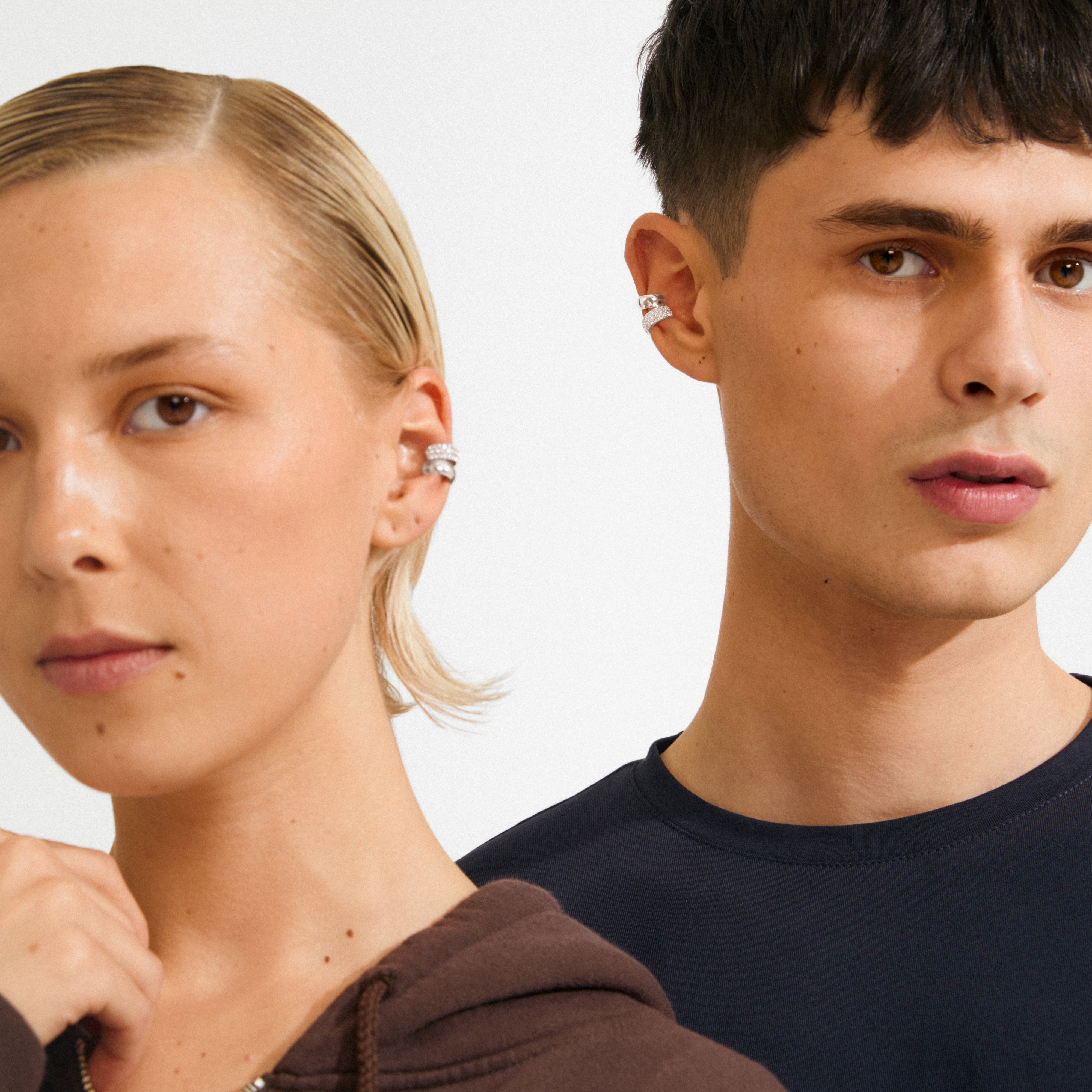 Two young adults wear HUDSYN ear cuffs, a 2-in-1 silver-plated set from Pilgrim, showcasing edgy and effortless style with multiple silver ear-cuff designs.