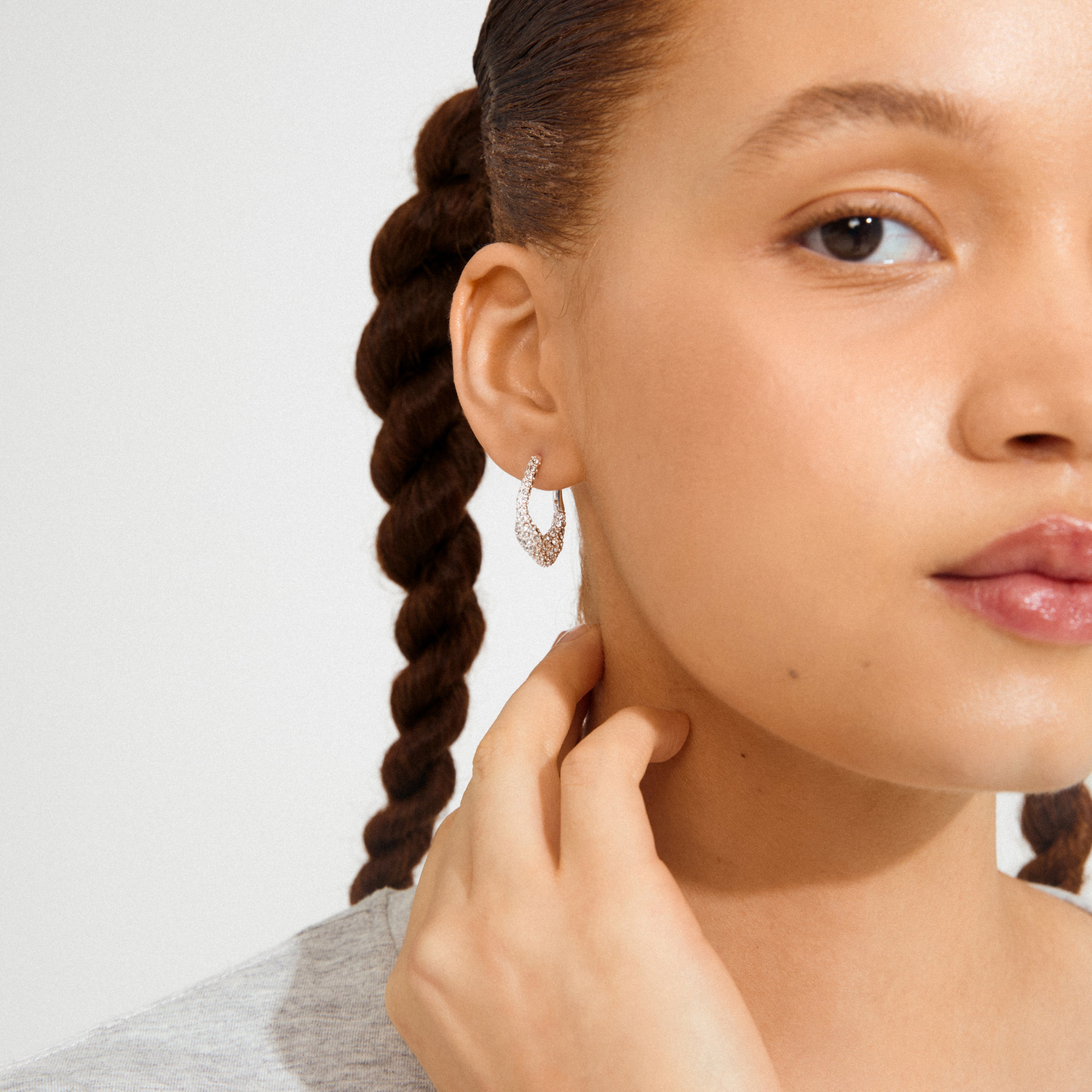 Young woman wears FENIX earrings, silver-plated with teardrop shape and sparkling crystals, showcasing elegance and attitude. Hair in braid, hand on neck.