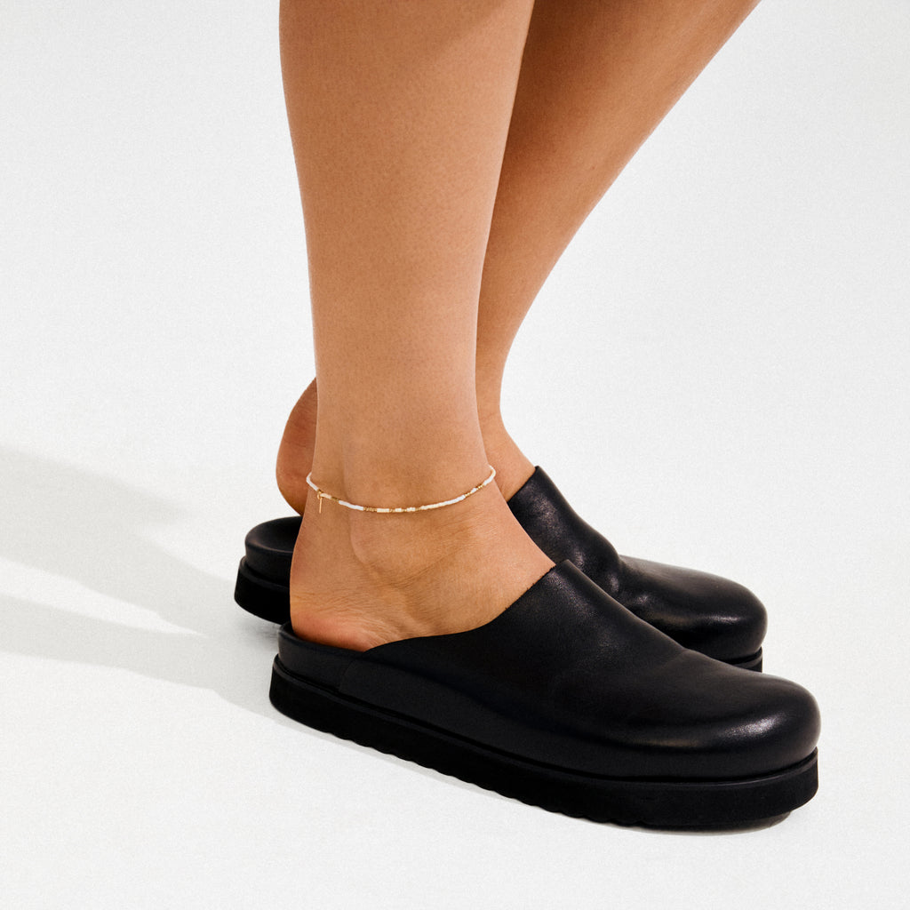 Black slip-on mules and Pilgrim's ALISON anklet with white and gold beads on ankle, reflecting boho vibes and effortless summer style.