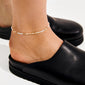 Close-up of an ankle wearing the ALISON ankle chain, featuring white and gold beads, paired with a black mule shoe. Perfect for summer's carefree boho vibes.