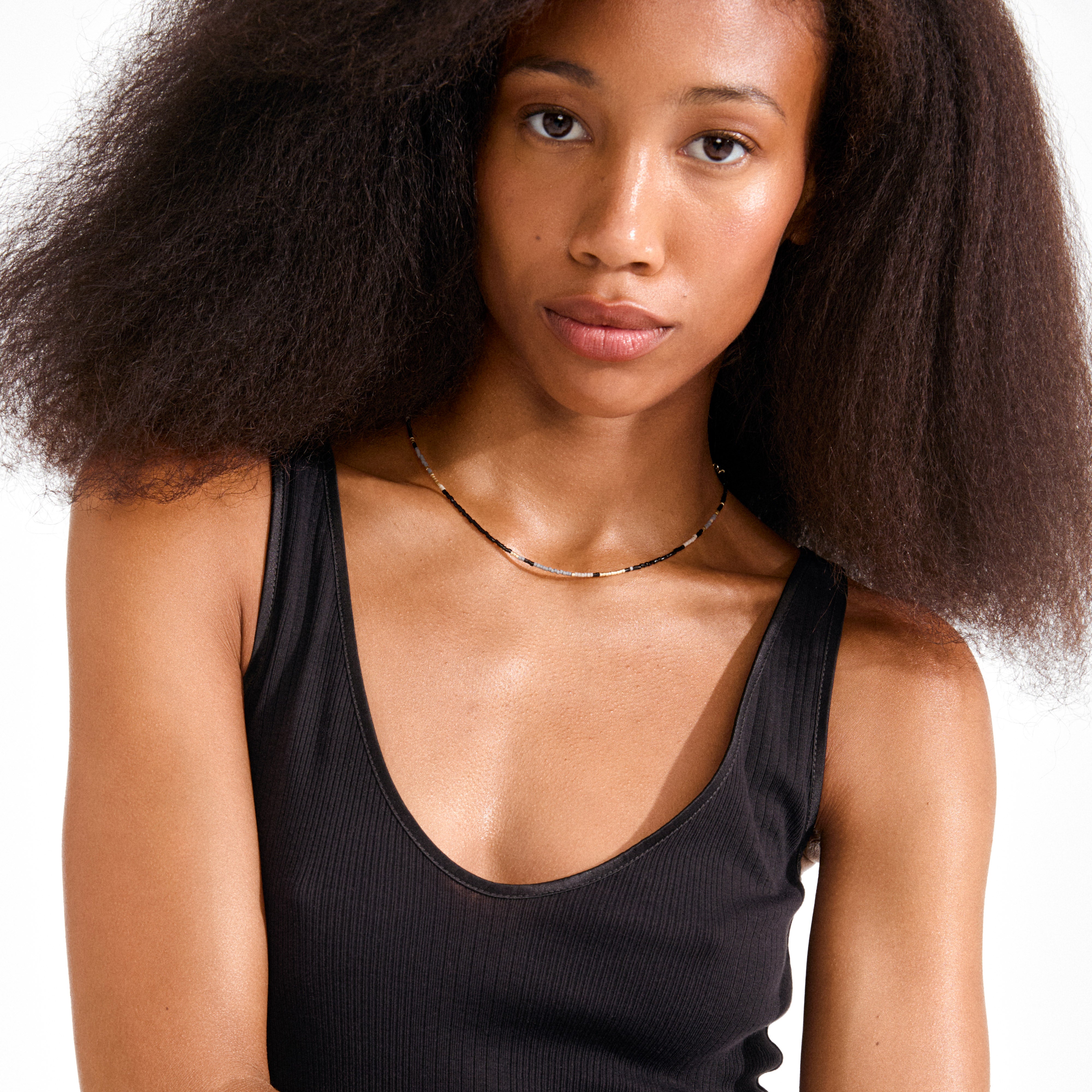 Young woman wearing the ALISON necklace by Pilgrim, featuring sleek black and gold tube-shaped beads, perfect for enhancing a casual yet chic summer look.