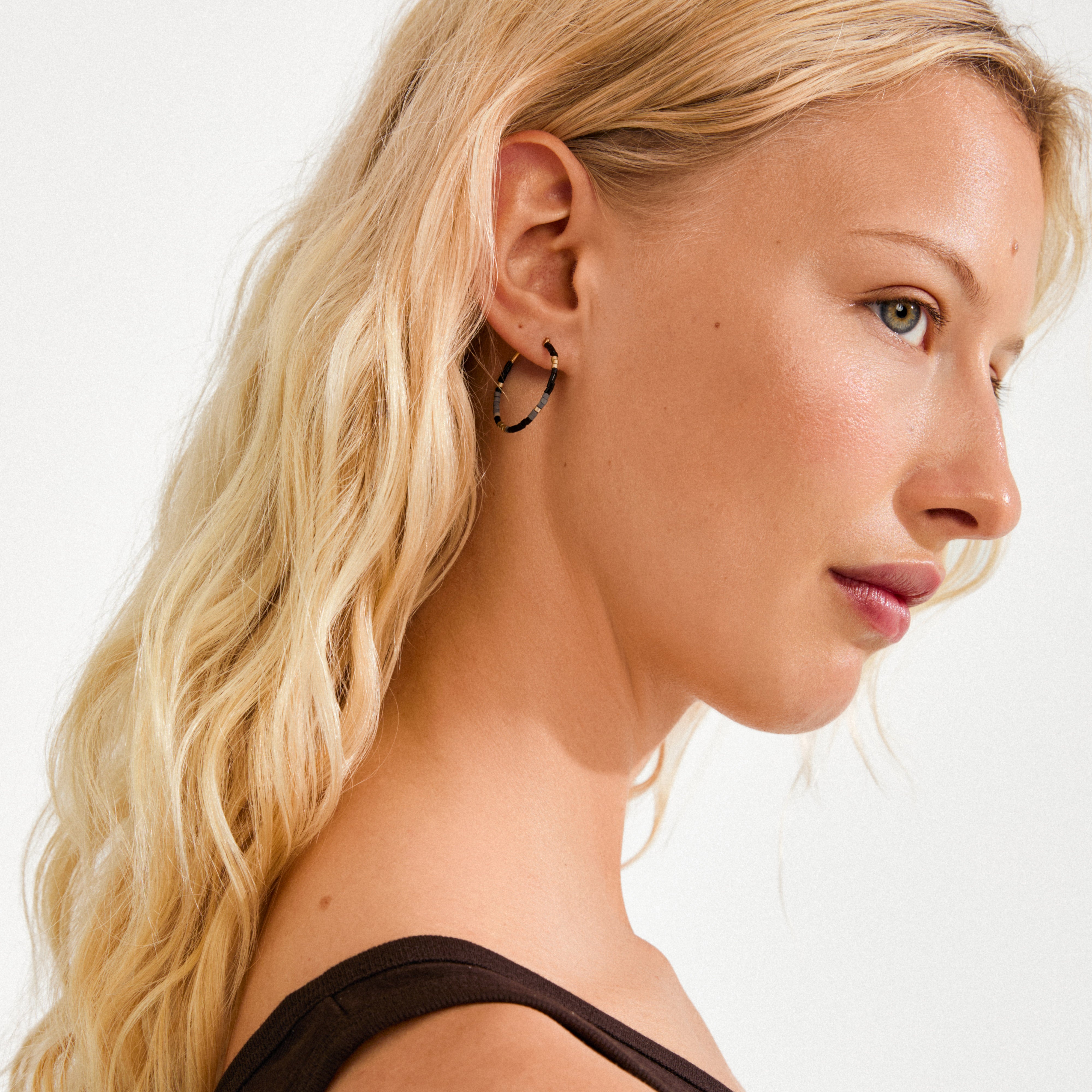 Young woman wearing Pilgrim's ALISON earrings featuring black and gold glass beads, styled with light blonde wavy hair for a chic, minimalist look.