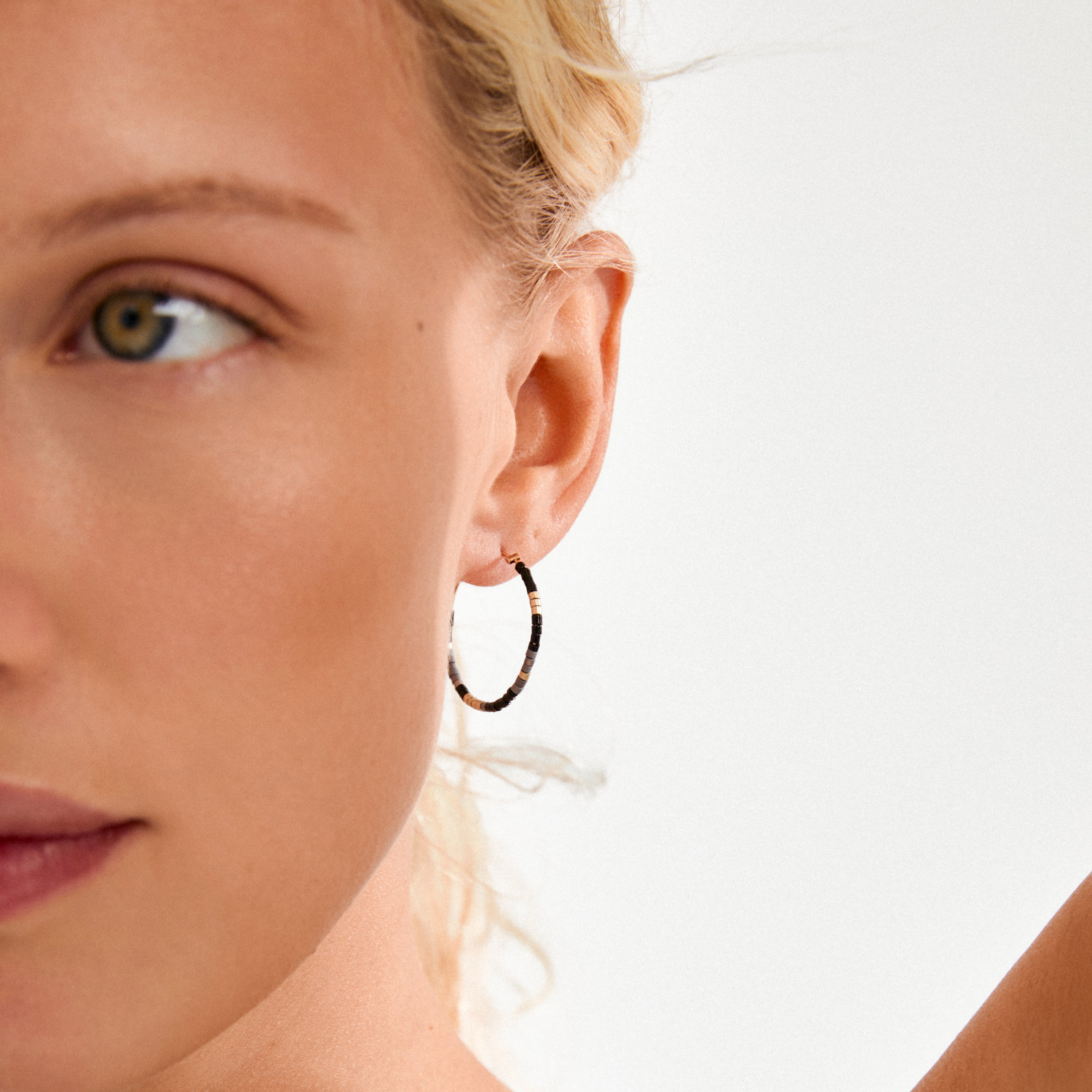 Close-up of ALISON earrings with black and gold beads, worn on a lightly freckled ear, showcasing Pilgrim's blend of boho glow and minimalist style.