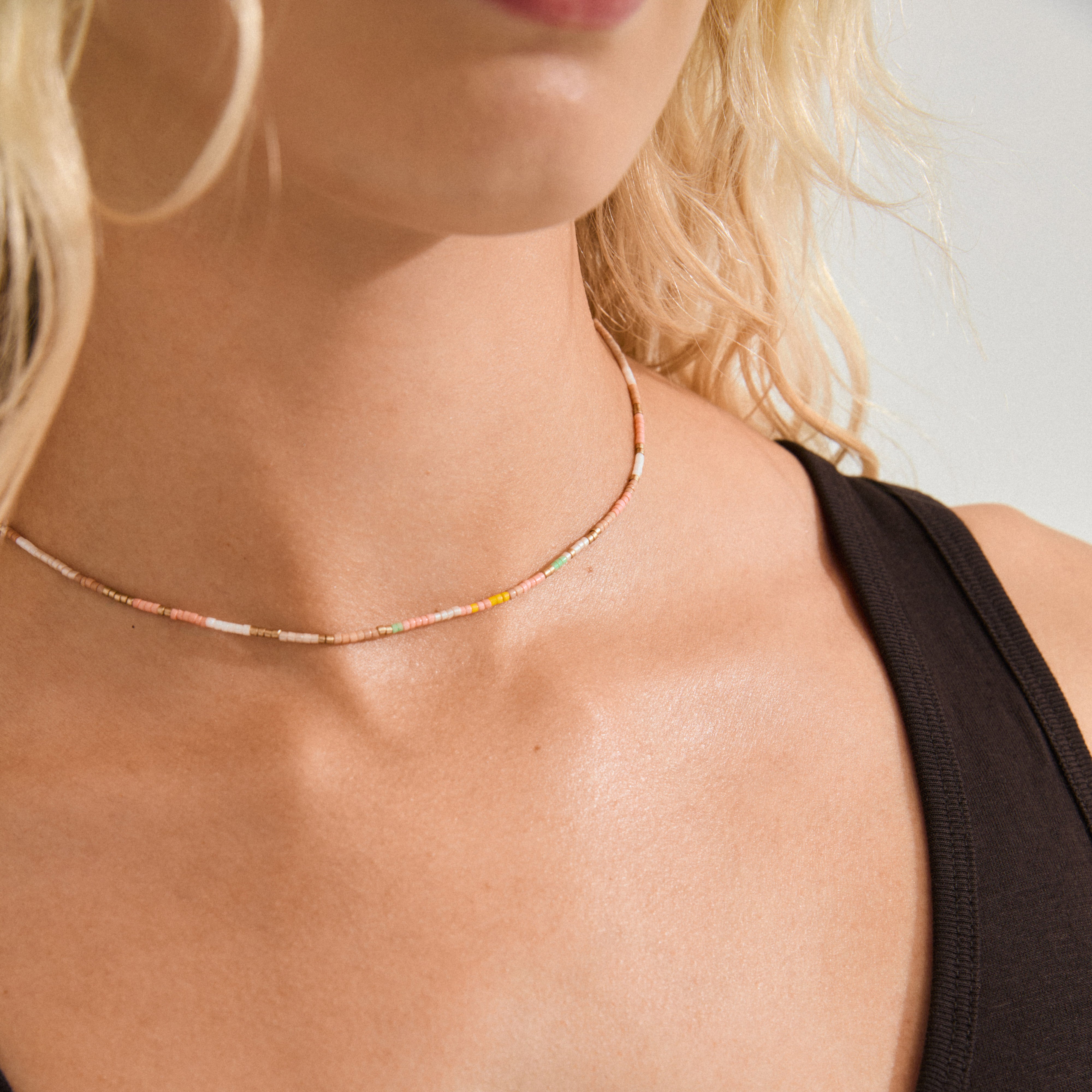 Close-up of a woman wearing the ALISON necklace, a multicolored, beaded choker from Pilgrim, paired with a large hoop earring and black tank top.