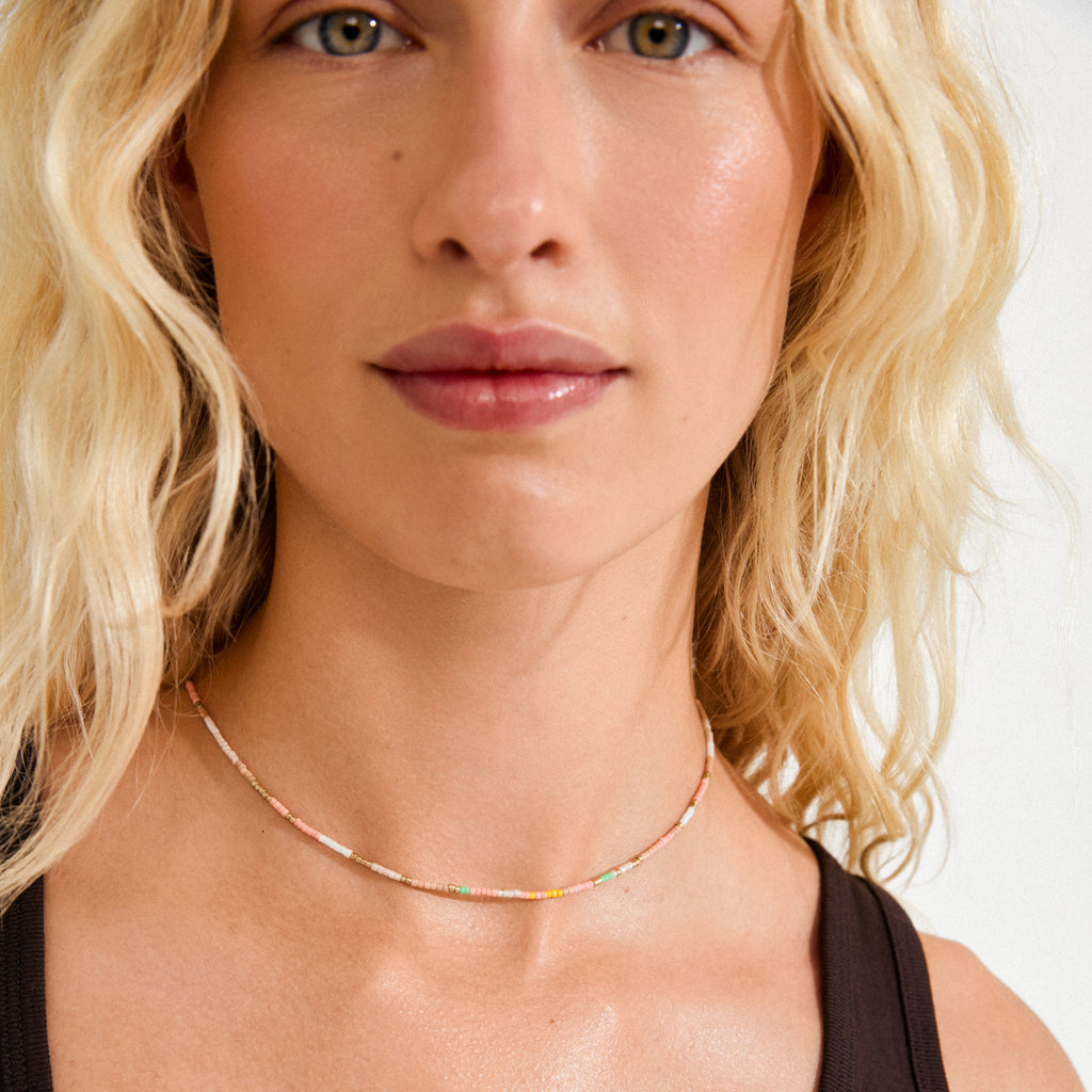 Close-up of a person wearing the ALISON necklace, a gold-plated choker featuring tiny multicolored beads, showcasing Pilgrim's vibrant, festival-inspired design.