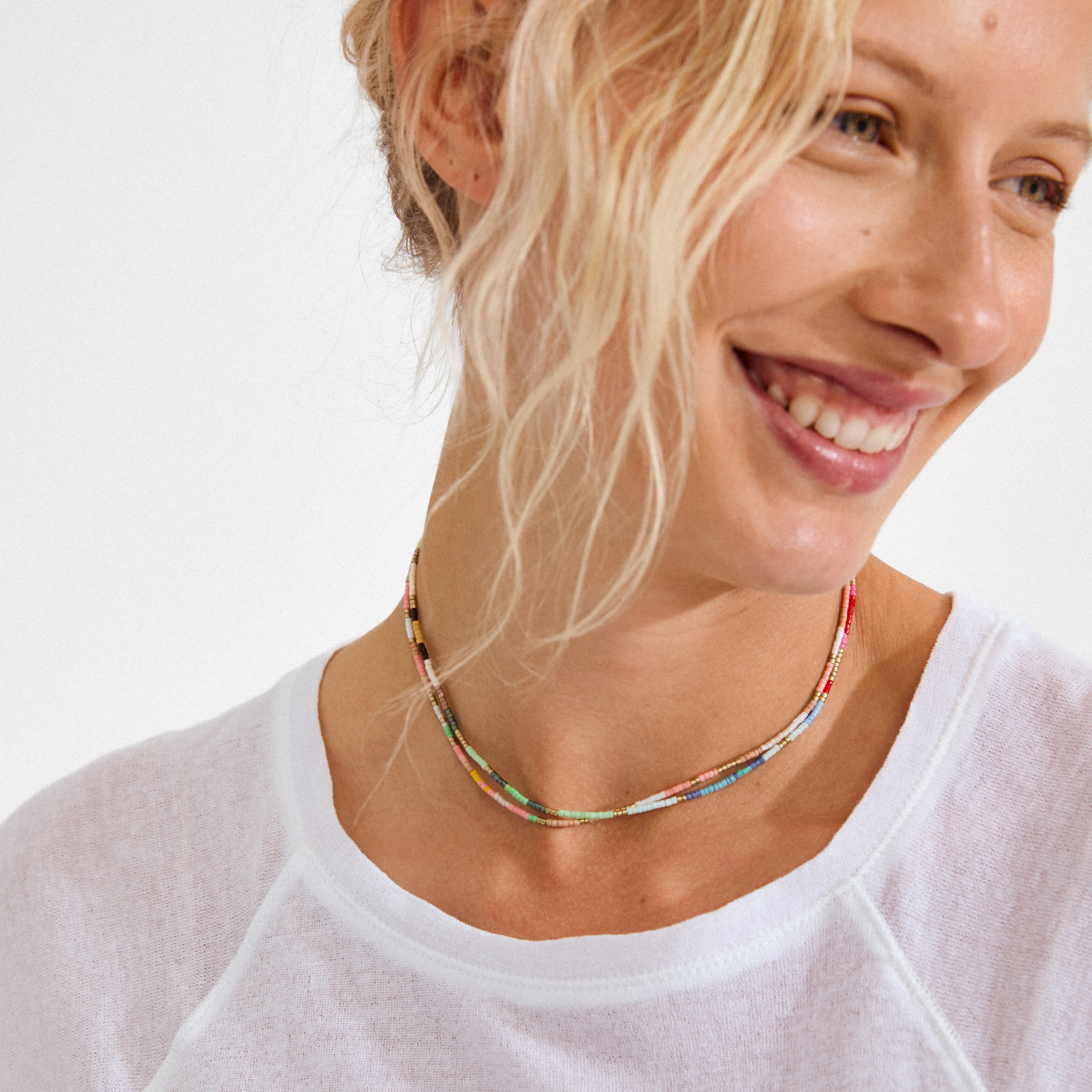 Smiling woman wearing the ALISON necklace, a vibrant double-strand of multicolored beads, highlighting Pilgrim's playful and trendy style.