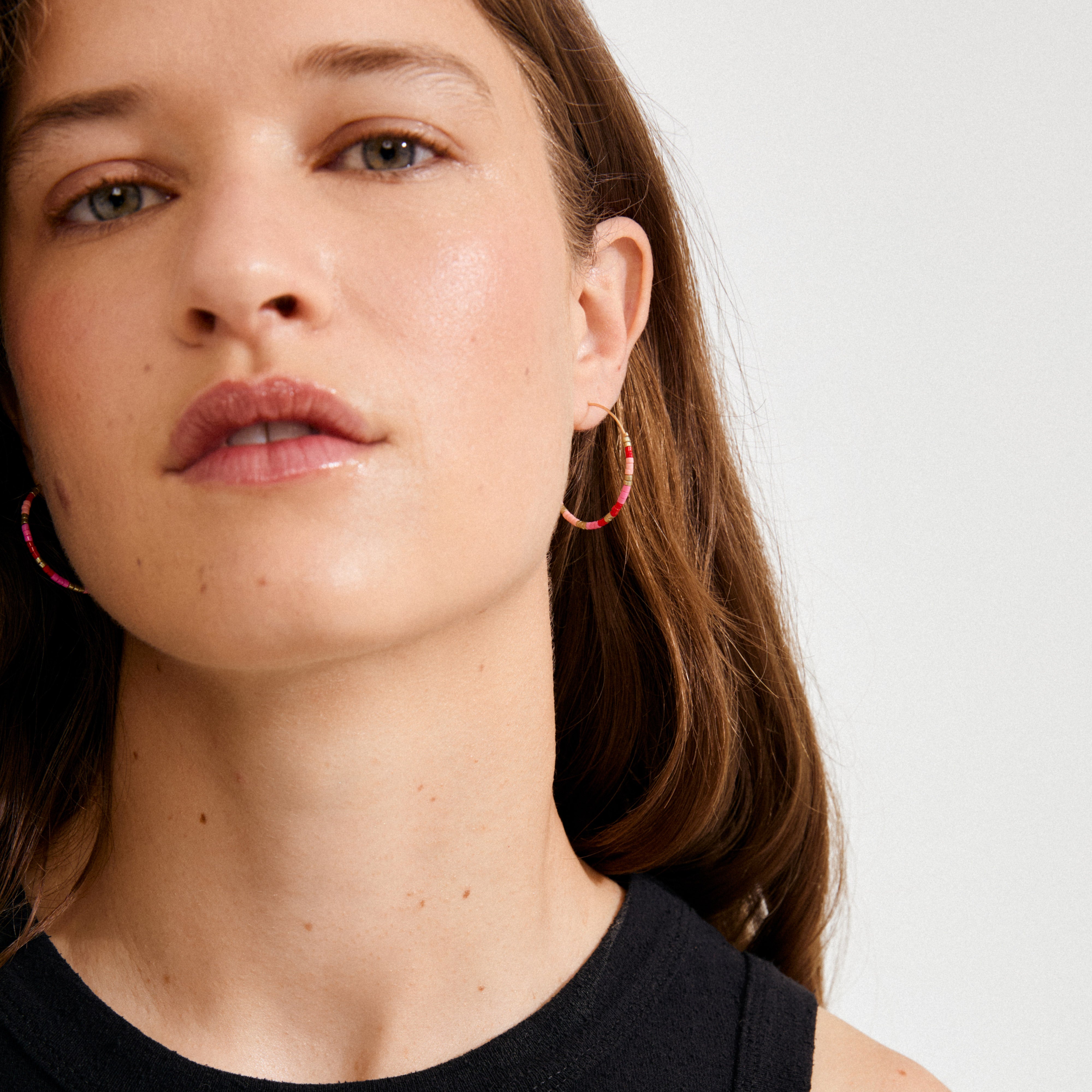 Young woman wearing Pilgrim's ALISON earrings—pink, gold-plated hoops with colorful beads, capturing a boho, festival vibe with a carefree and trendy style.