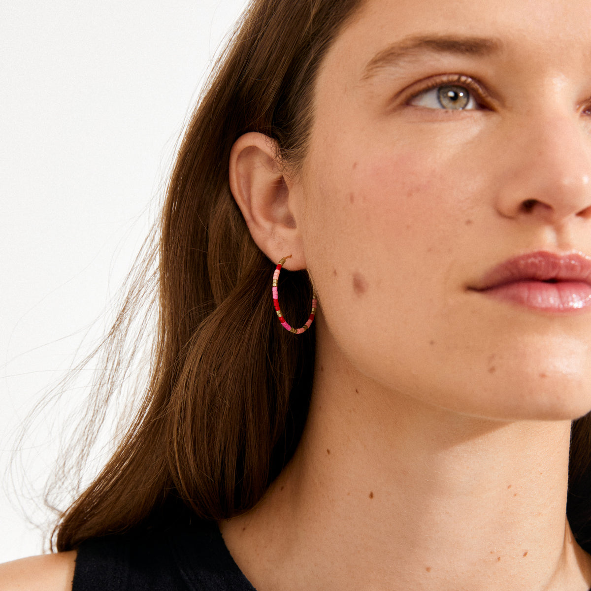 Close-up of a woman wearing ALISON earrings from Pilgrim, featuring medium-sized hoops with pink, red, and gold beads, capturing a boho and vibrant style.
