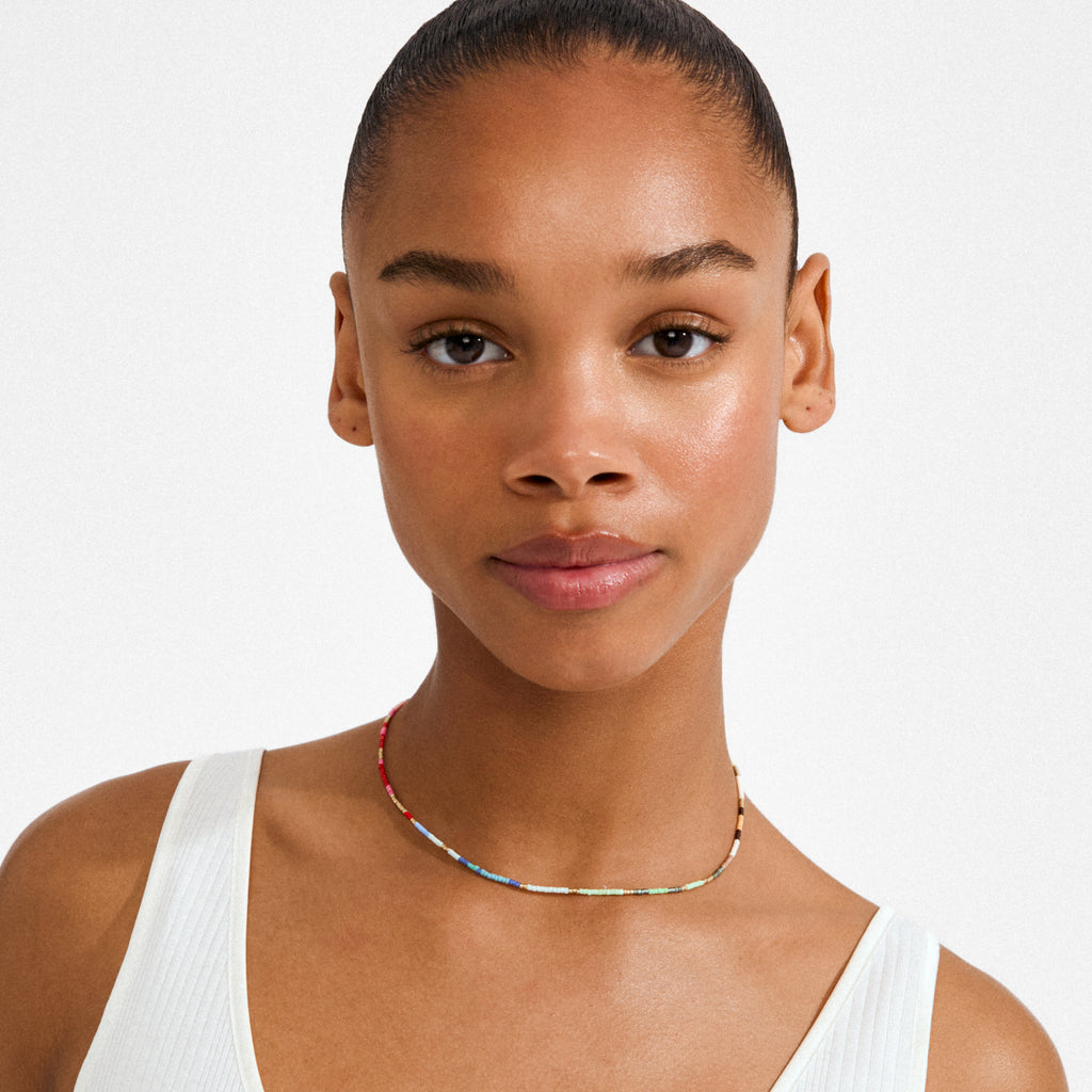 Young woman wearing the ALISON necklace multi, gold-plated, featuring vibrant tube-shaped beads, styled with a white ribbed tank top, showcasing Pilgrim's playful design.