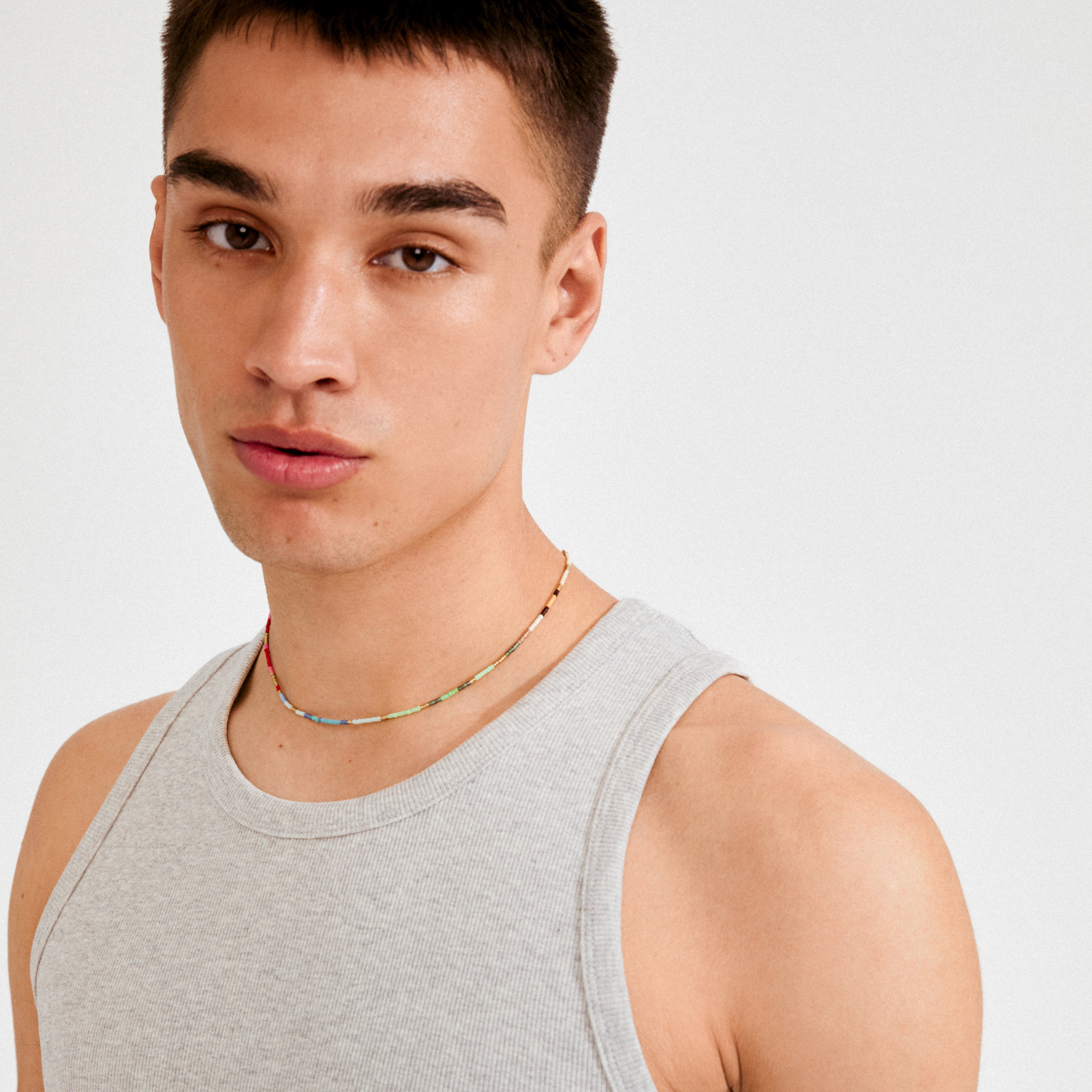 Young man wearing the ALISON necklace multi, gold-plated, featuring vibrant tube-shaped glass beads, showcasing a playful, festival-inspired style.