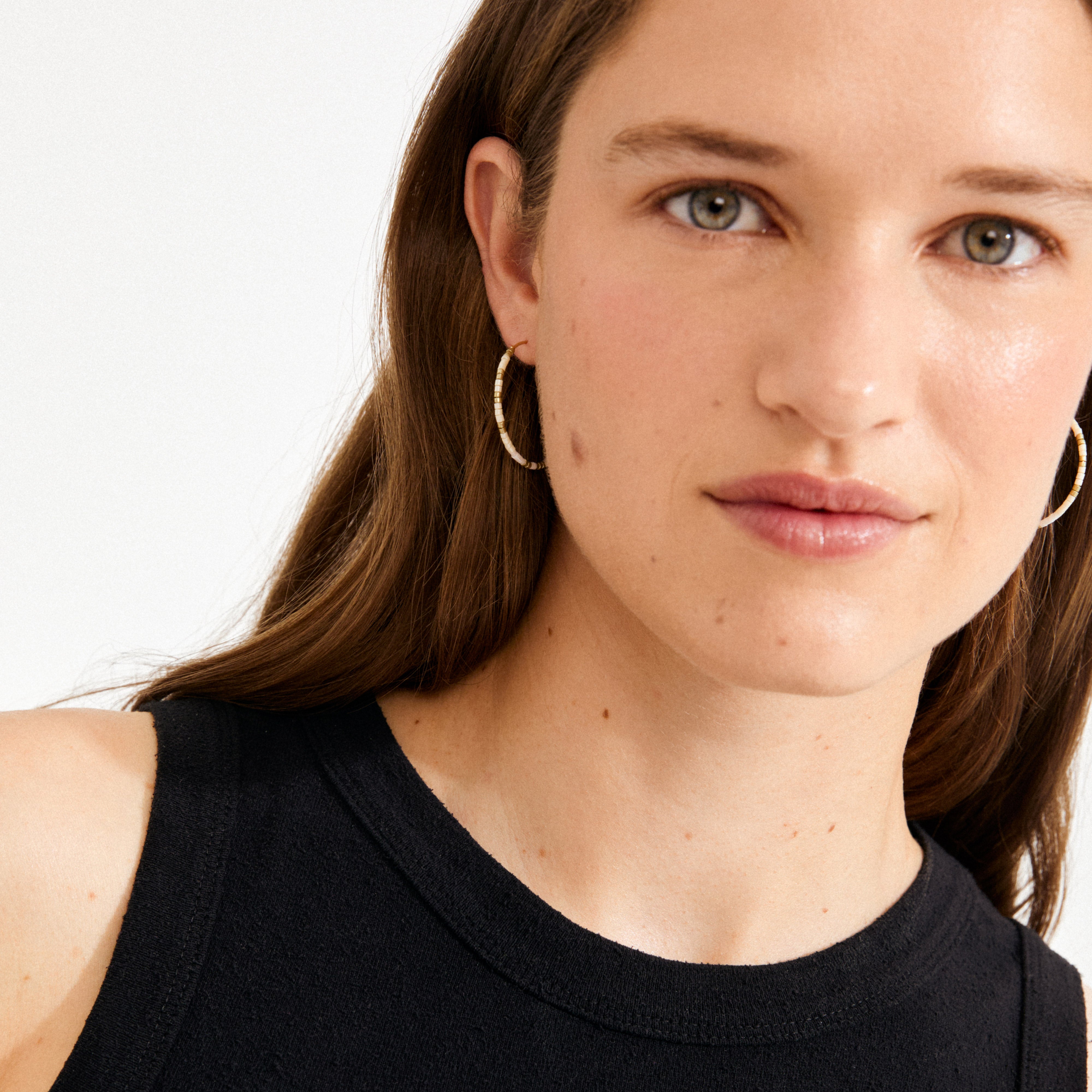 Young woman wearing ALISON earrings, white and gold-plated hoops with minimalist design, showcasing Pilgrim's boho-inspired charm and lightweight, comfortable elegance.