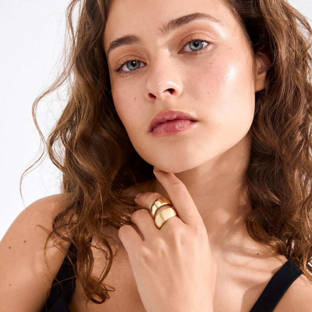 Young woman showcases ALMA ring gold-plated, featuring chunky, polished design on index and middle fingers, embodying minimalist elegance with sleek, satin-matte finishes.