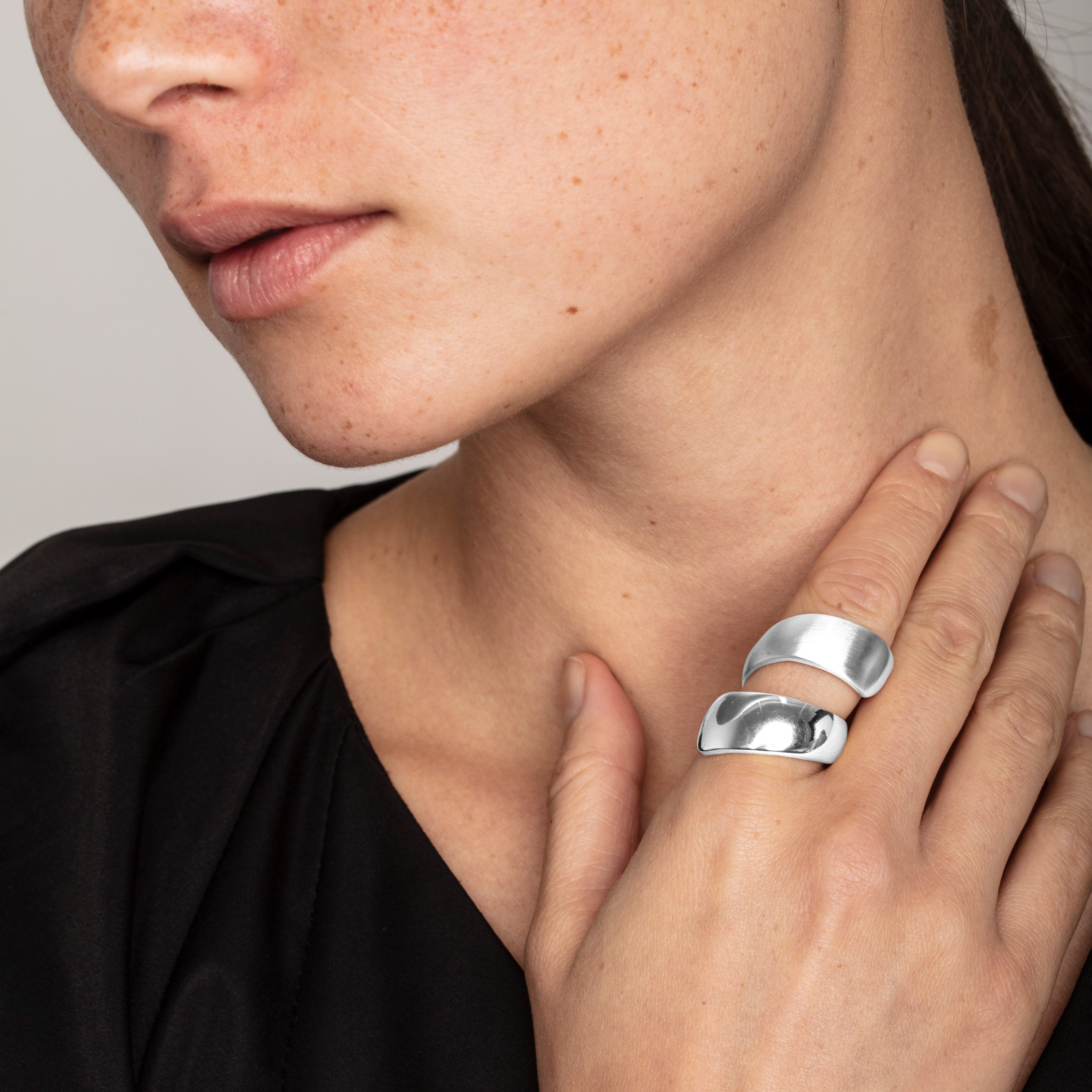 Silver ALMA ring, twining twice around a woman's finger, showcasing its shiny and matte surfaces, embodying stylish determination and elegance.