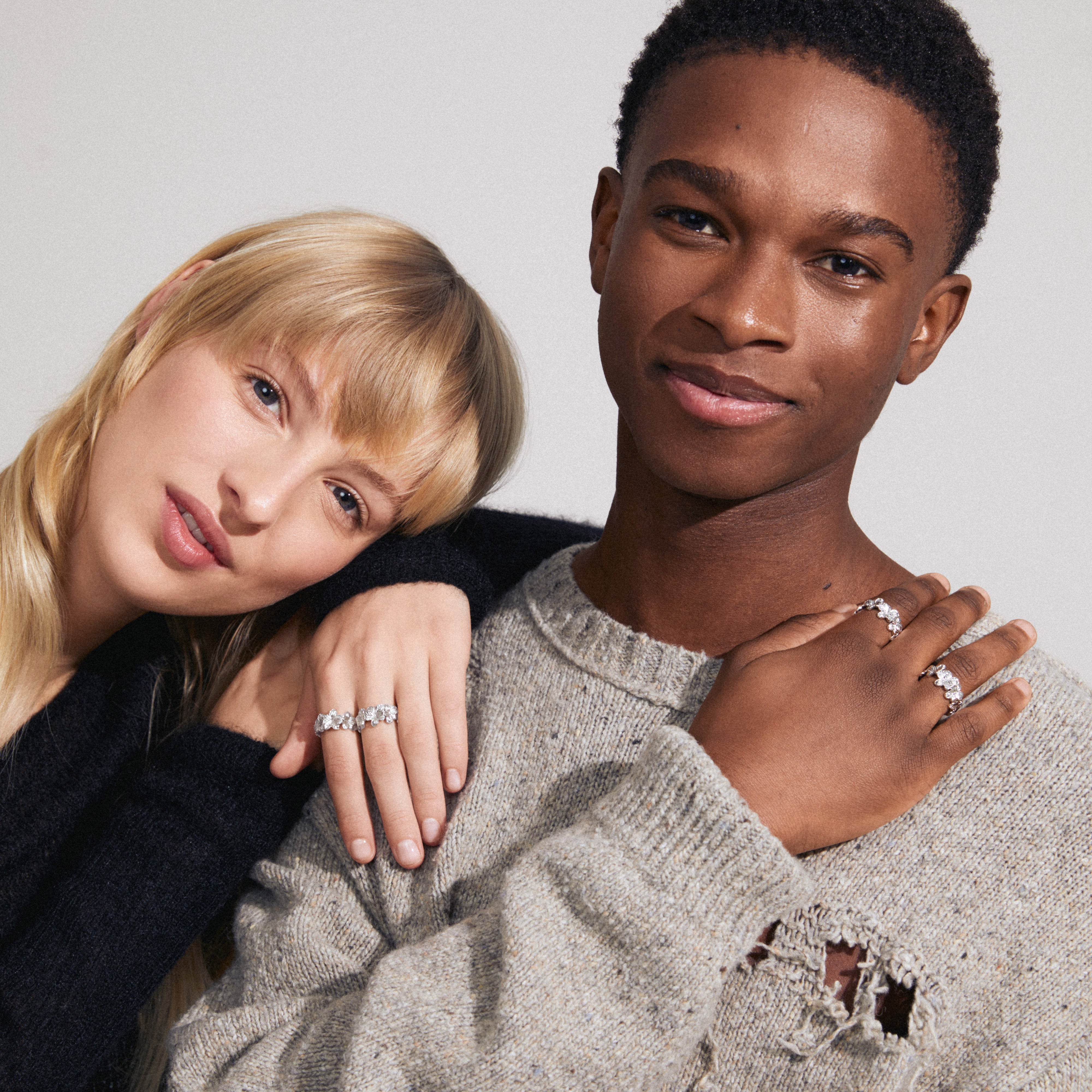 Man and woman showcasing CHARMAINE rings 2-in-one set, silver-plated, with elegant floral motifs from Pilgrim. Rings are stacked and worn on woman's hand.