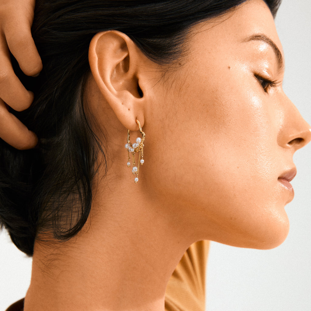 JASPER earrings gold-plated: Delicate hoop with clustered pearls and fine chains, reflecting a dreamcatcher-inspired design, worn by a woman with dark hair.