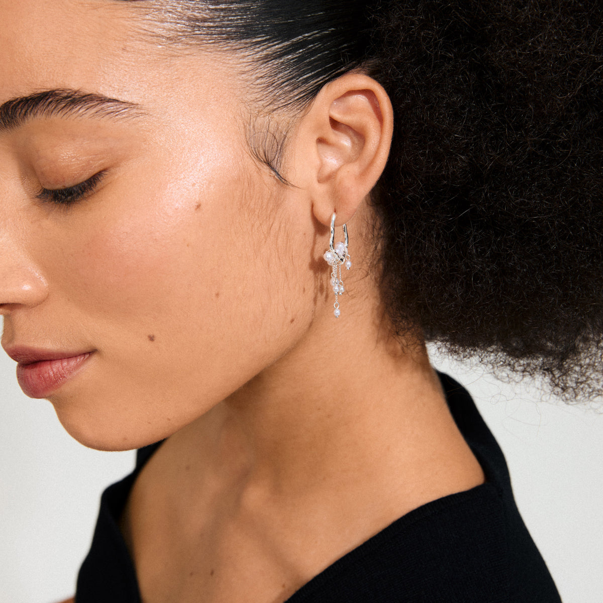 Close-up of a person wearing JASPER earrings, silver-plated hoops with beads and chains, showcasing an organic, dreamcatcher-inspired design by Pilgrim.