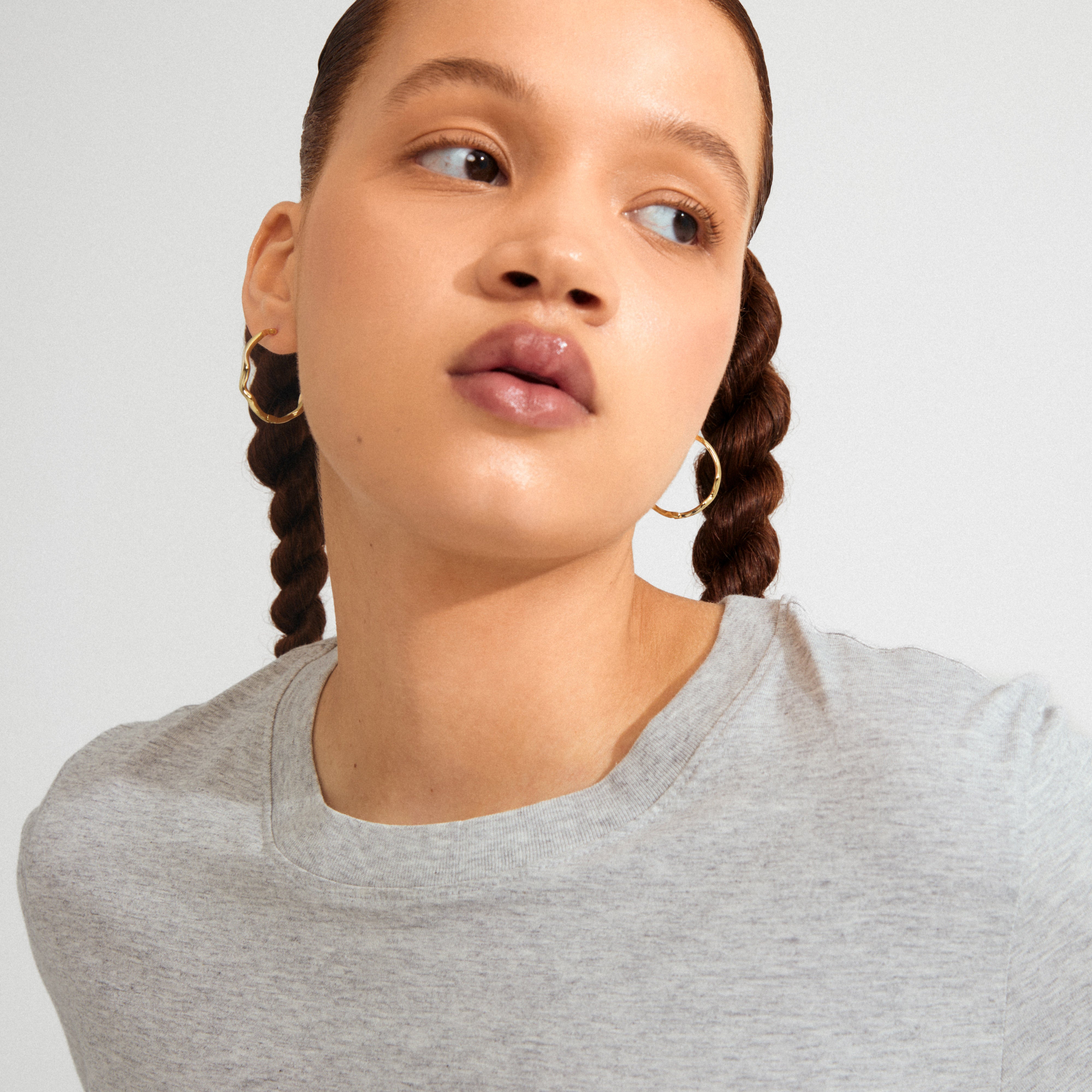 Young woman wearing Pilgrim's LARKIN earrings, gold-plated with a wavy silhouette, showcasing their minimalist yet impactful design against a softly lit background.