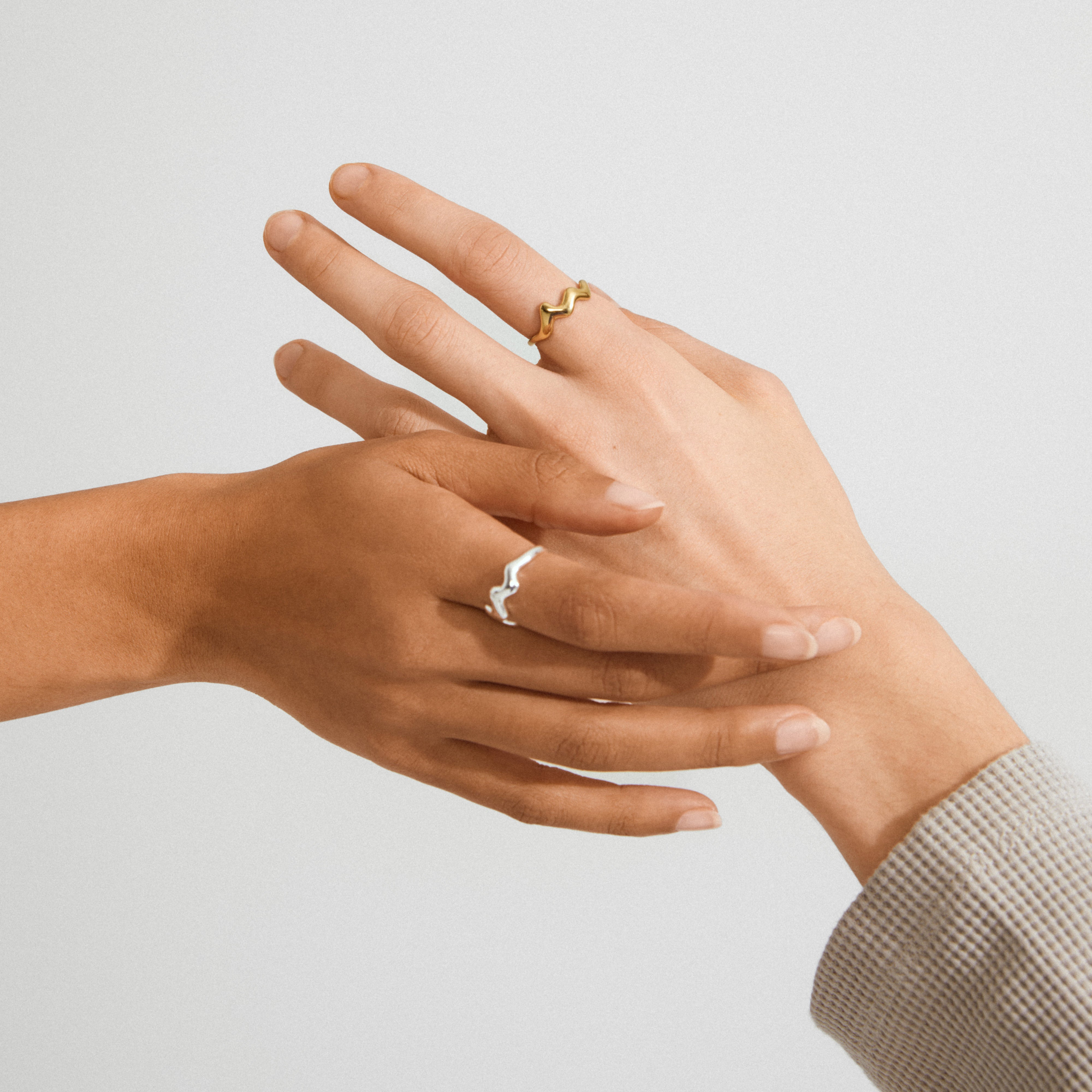 Hands display Pilgrim's LARKIN gold-plated ring, featuring a wavy, fluid design. The ring's minimalist elegance is ideal for stacking or solo wear.