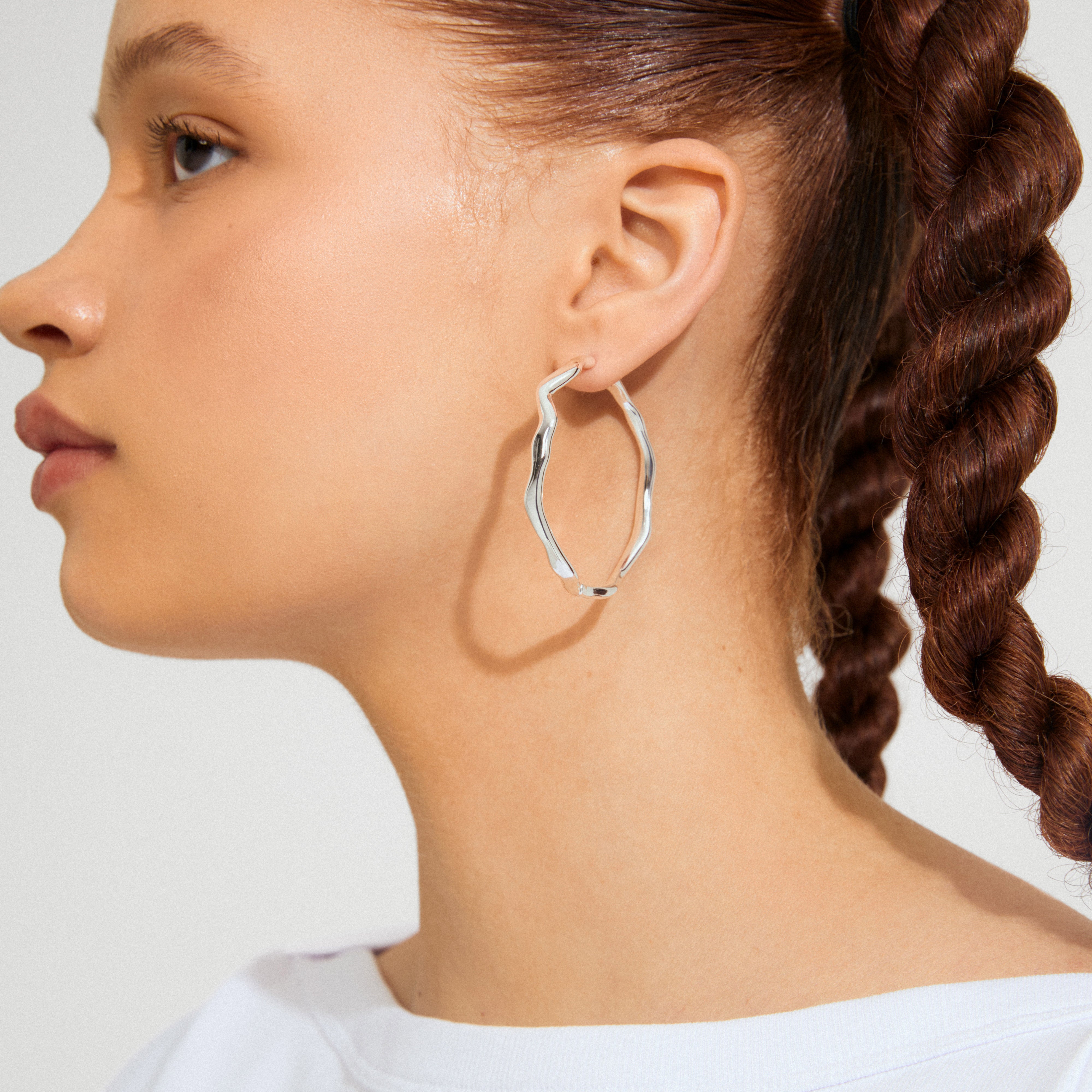 Side profile highlighting LARKIN silver-plated earrings by Pilgrim, featuring a wavy, sculptural design, worn by a person with a braided hairstyle.