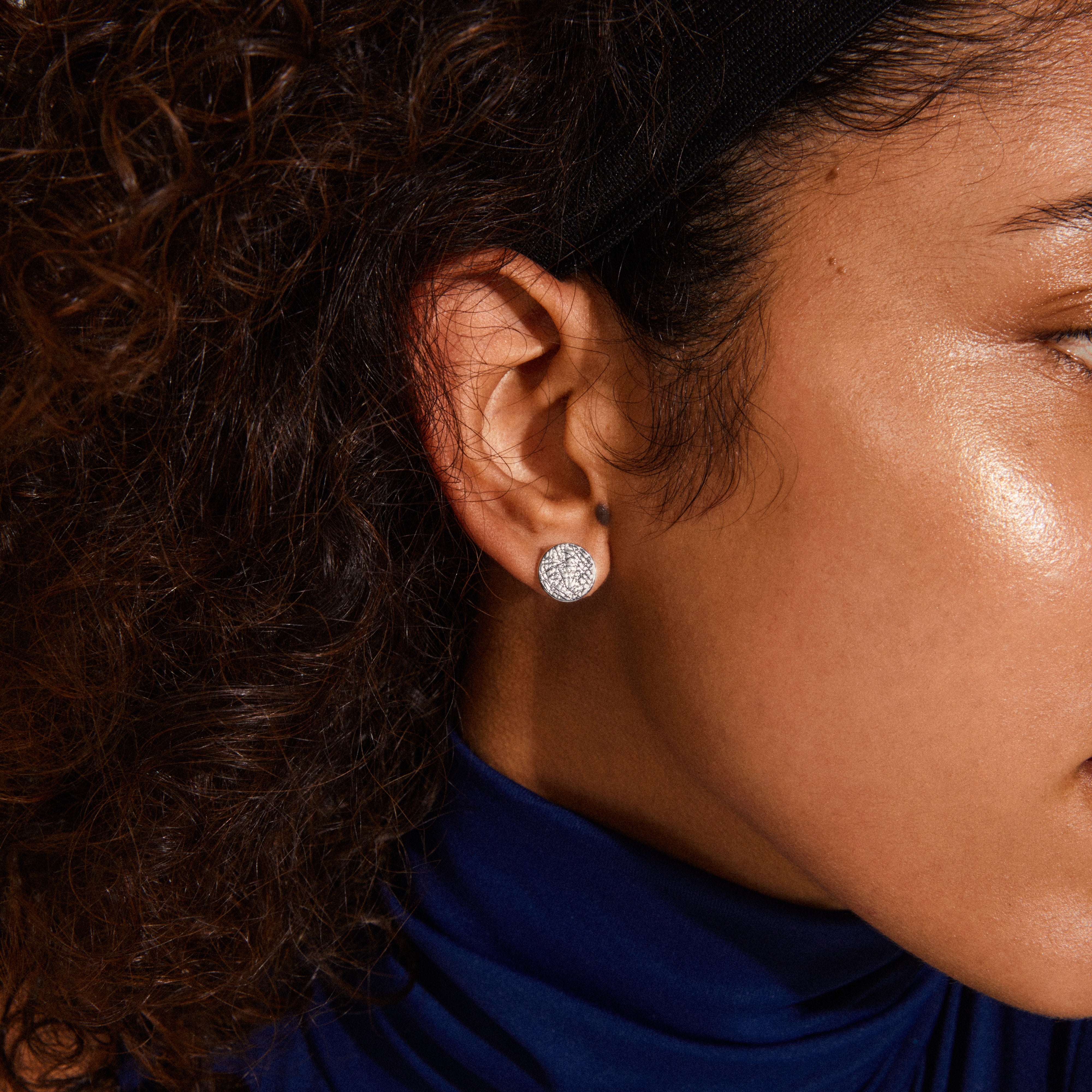 WYNONNA rustic earrings, silver-plated, with a raw, textured design, worn by a woman with curly hair, showcasing an edgy yet elegant style.