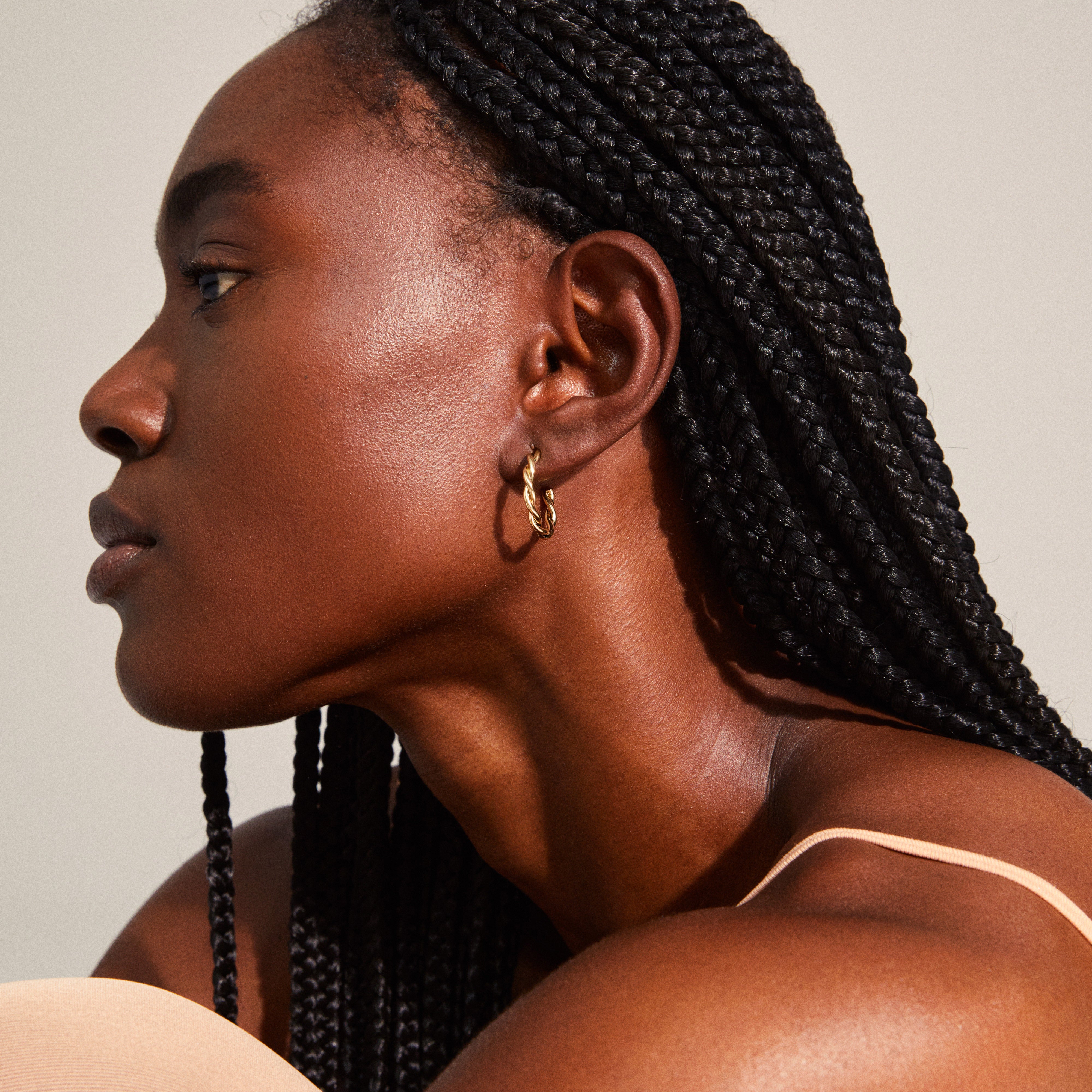 NAJA twisted hoop earrings in gold-plated finish, showcased on a woman with braided hair, highlighting their elegant, light-catching twisted design.