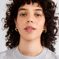 Young adult wearing MADDIE chunky hoop earrings, gold-plated, with a glossy finish, highlighting their bold, stylish appeal against a simple gray tee.