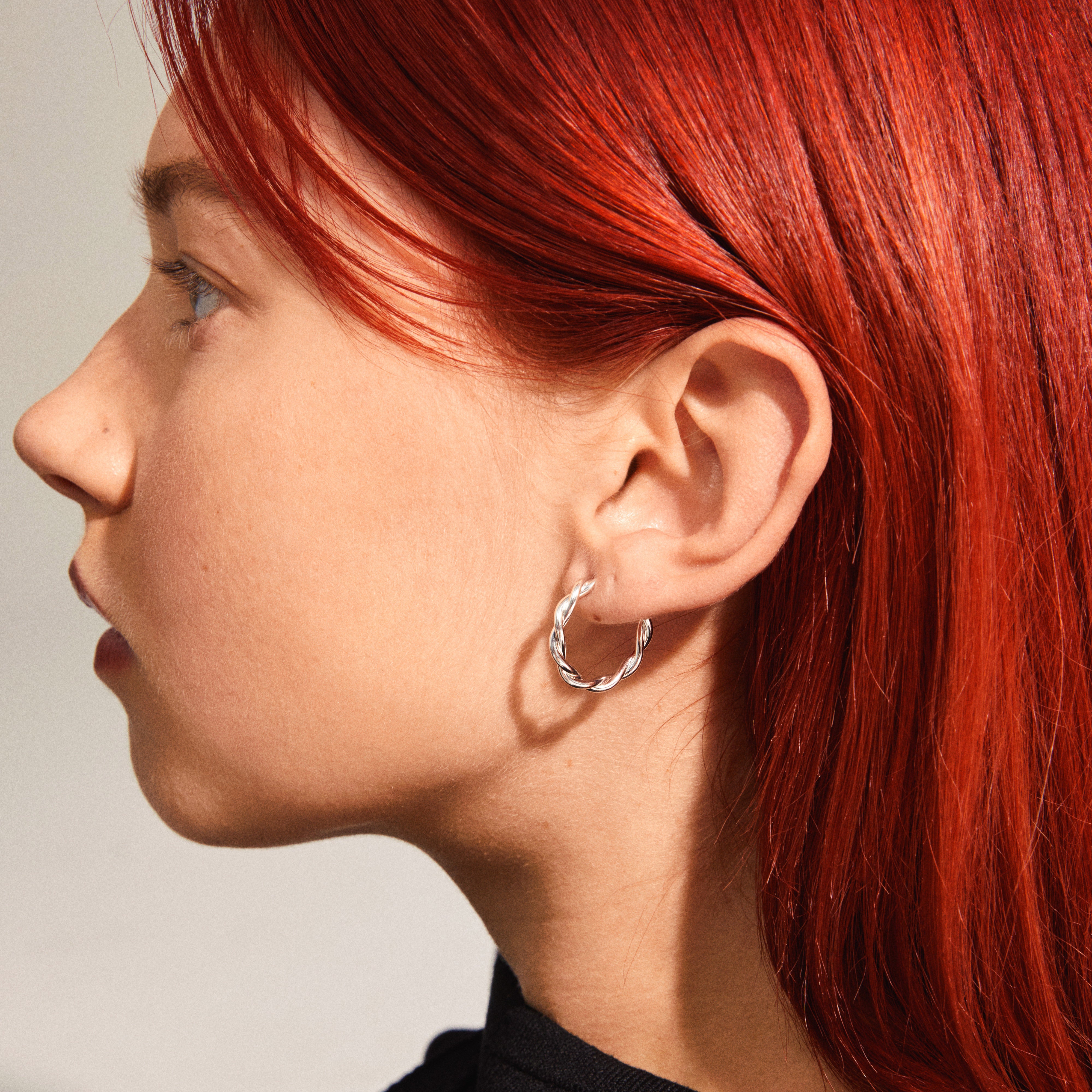 NAJA twisted hoop earrings, silver-plated, showcased on a woman's ear; the hoops feature a light-catching twisted design for an elegant touch.