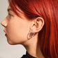 NAJA twisted hoop earrings, silver-plated, showcased on a woman's ear; the hoops feature a light-catching twisted design for an elegant touch.