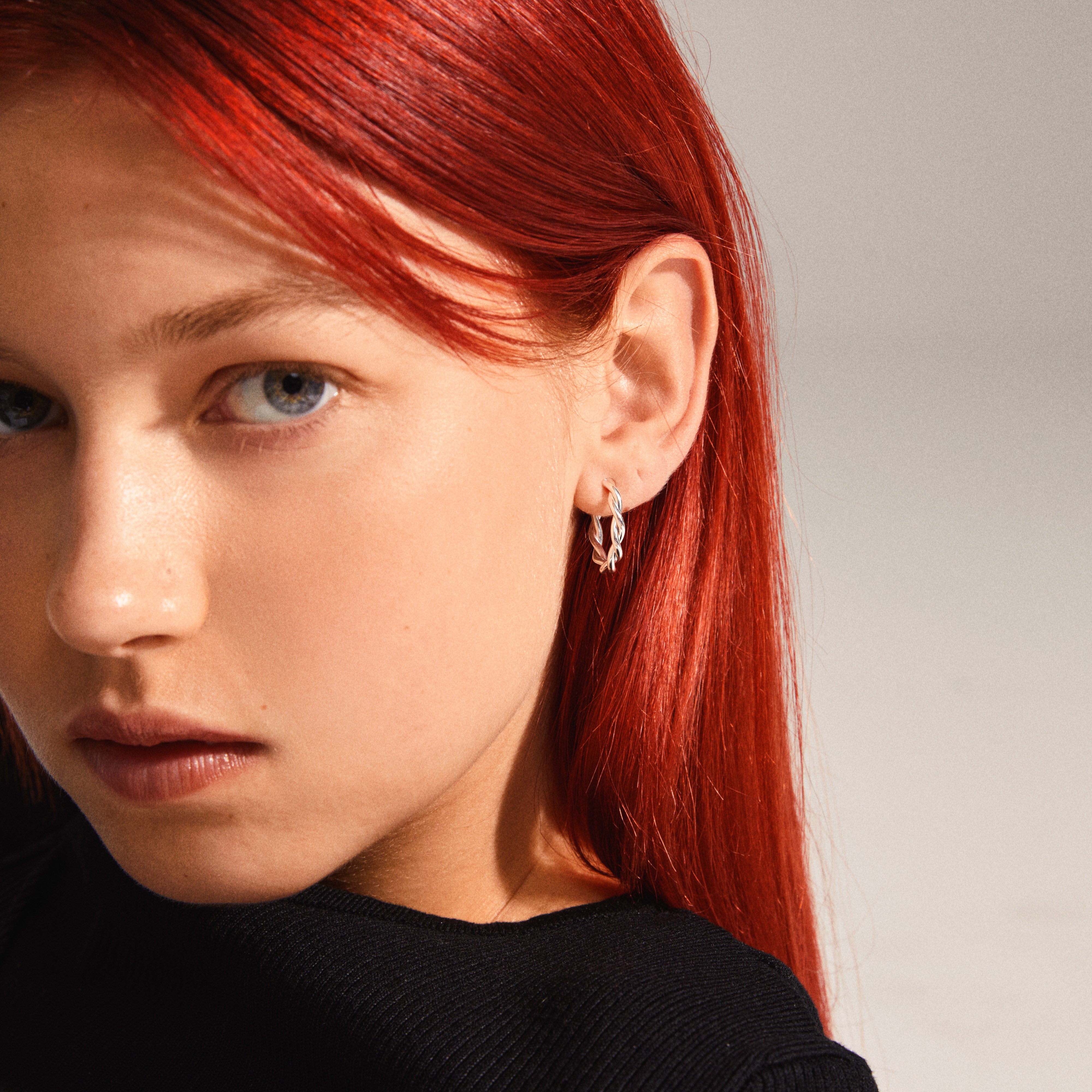 NAJA twisted hoop earrings in silver-plated design, featuring elegant twisted details, worn by a red-haired woman, emphasizing the jewelry's stylish and modern appeal.