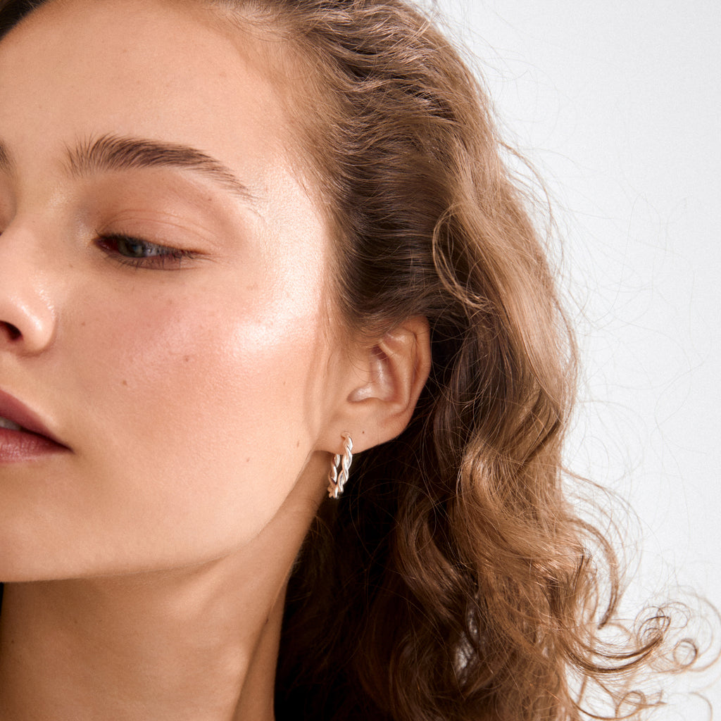 Close-up of a young woman wearing silver-plated NAJA twisted hoop earrings, highlighting the hoops' sculptural design and playful elegance. Perfect for adding style to any look.