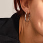 Close-up of a person wearing NAJA large silver-plated hoop earrings with a twisted design, showcasing elegant light reflections, paired with a black knit top.
