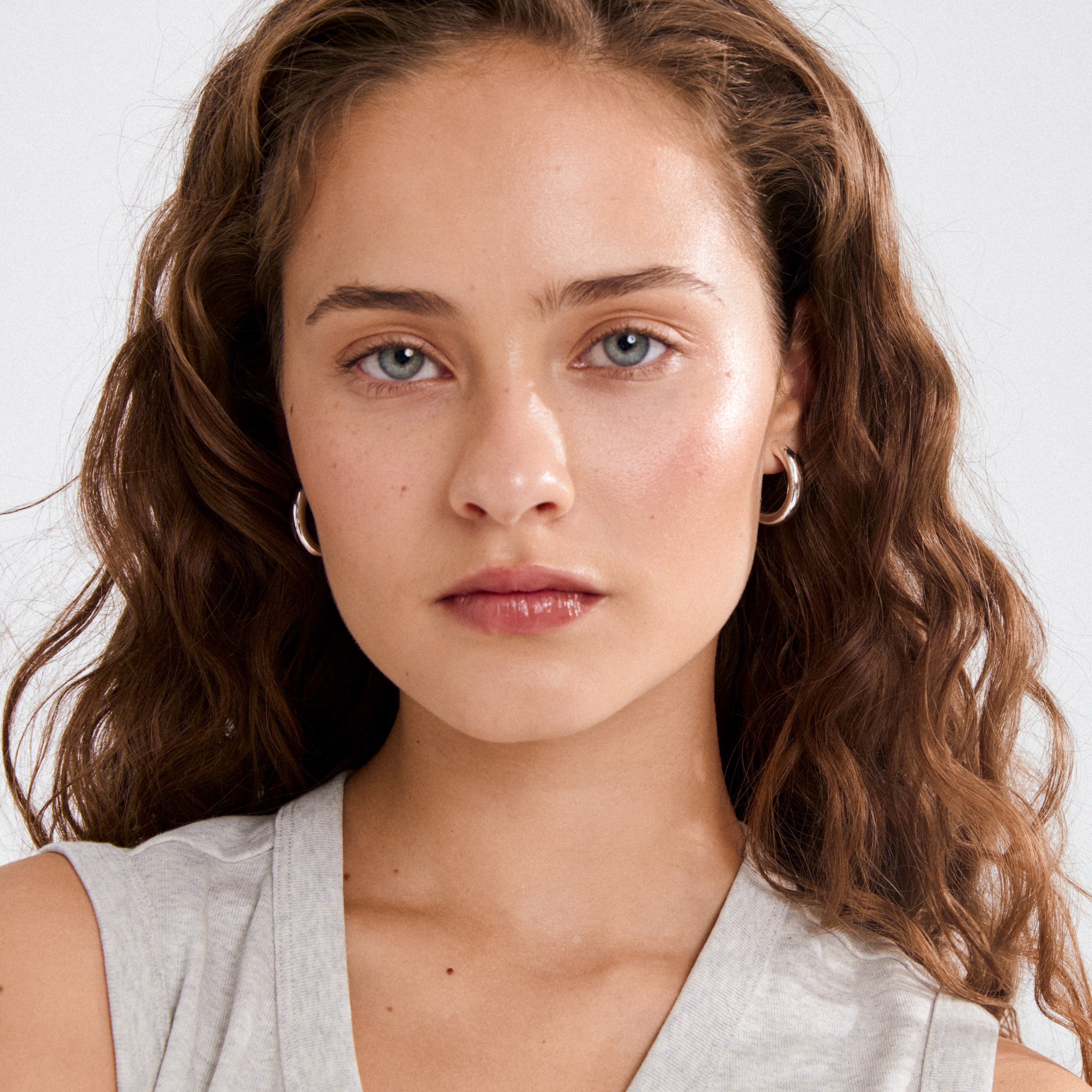 Close-up of a woman wearing MADDIE chunky hoop earrings, silver-plated, showcasing their glossy finish and stylish, bold design.