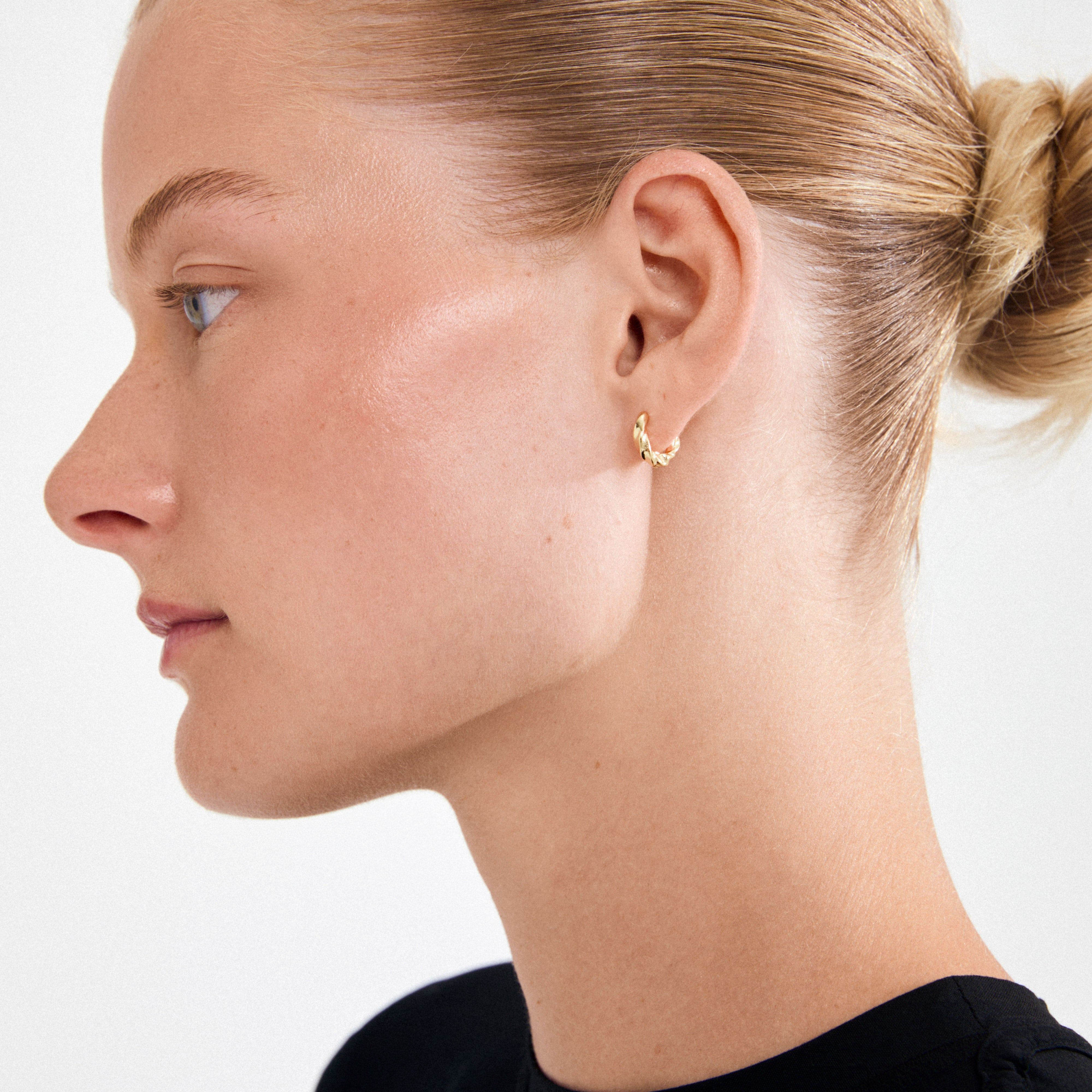 Side profile of a woman wearing Pilgrim's TAFFY small swirl gold-plated hoop earring, showcasing its elegant, nature-inspired design against a minimalist white background.