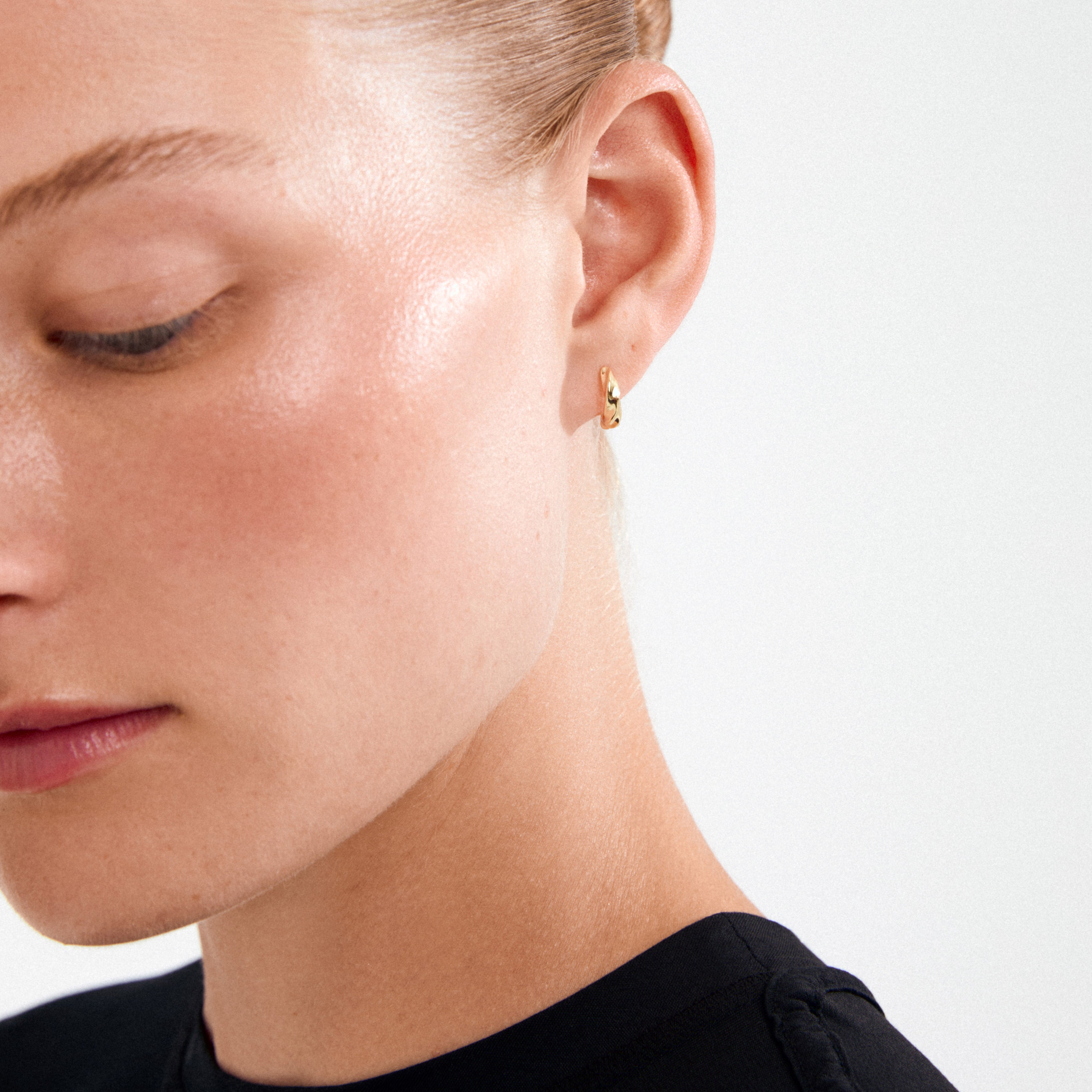 Woman wearing Pilgrim’s TAFFY small swirl hoop earrings, gold-plated, showcasing a sculptural design inspired by nature. Hair pulled back to highlight the earring's handcrafted elegance.