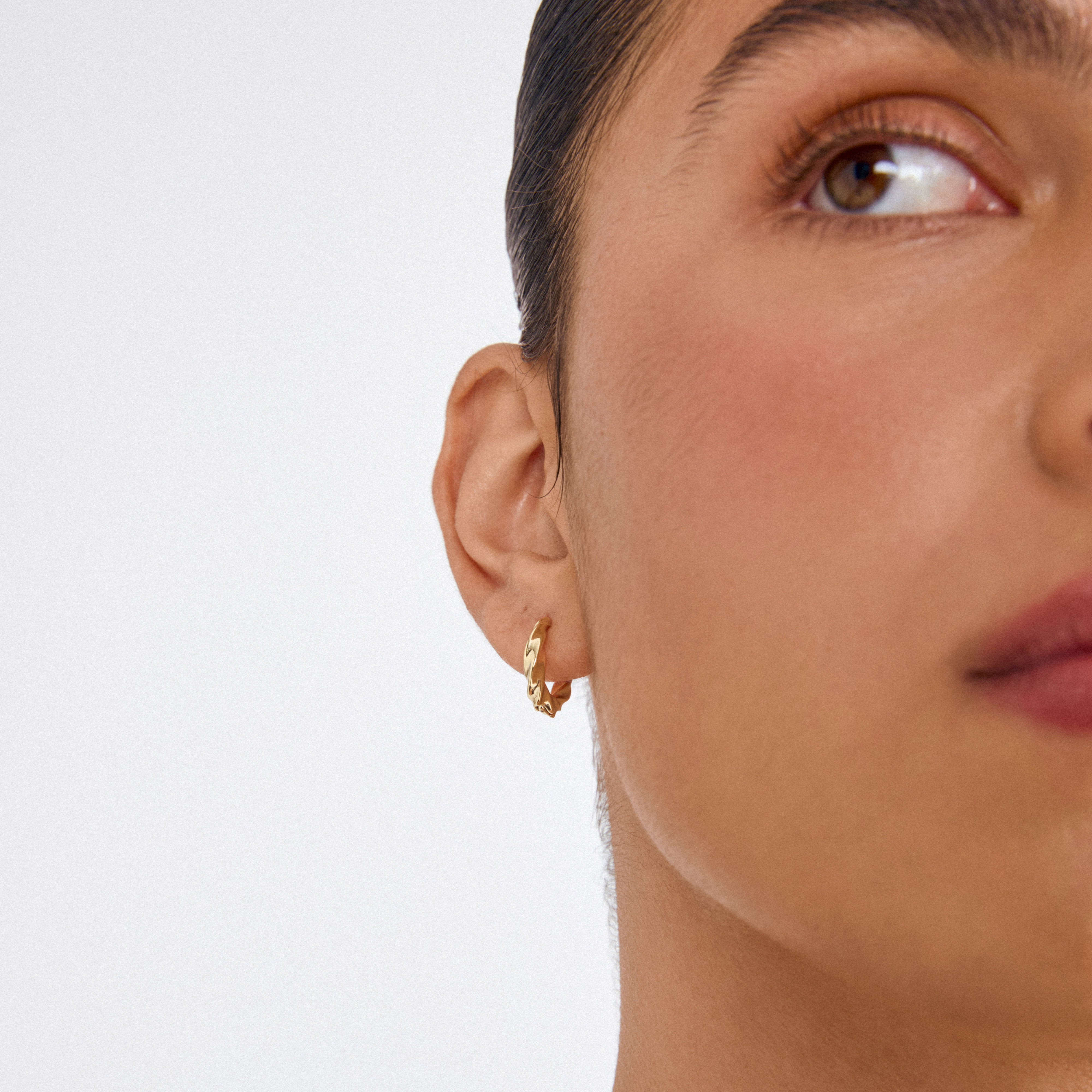 Close-up of a person's ear adorned with Pilgrim's TAFFY medium size swirl hoop earrings, gold-plated, showcasing their nature-inspired, vintage twist design.