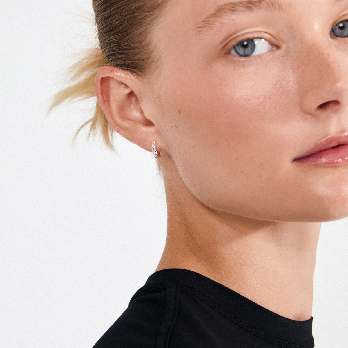 Close-up of a person's ear wearing Pilgrim's TAFFY small swirl hoop earrings, silver-plated, showcasing their handcrafted, nature-inspired design against a white background.