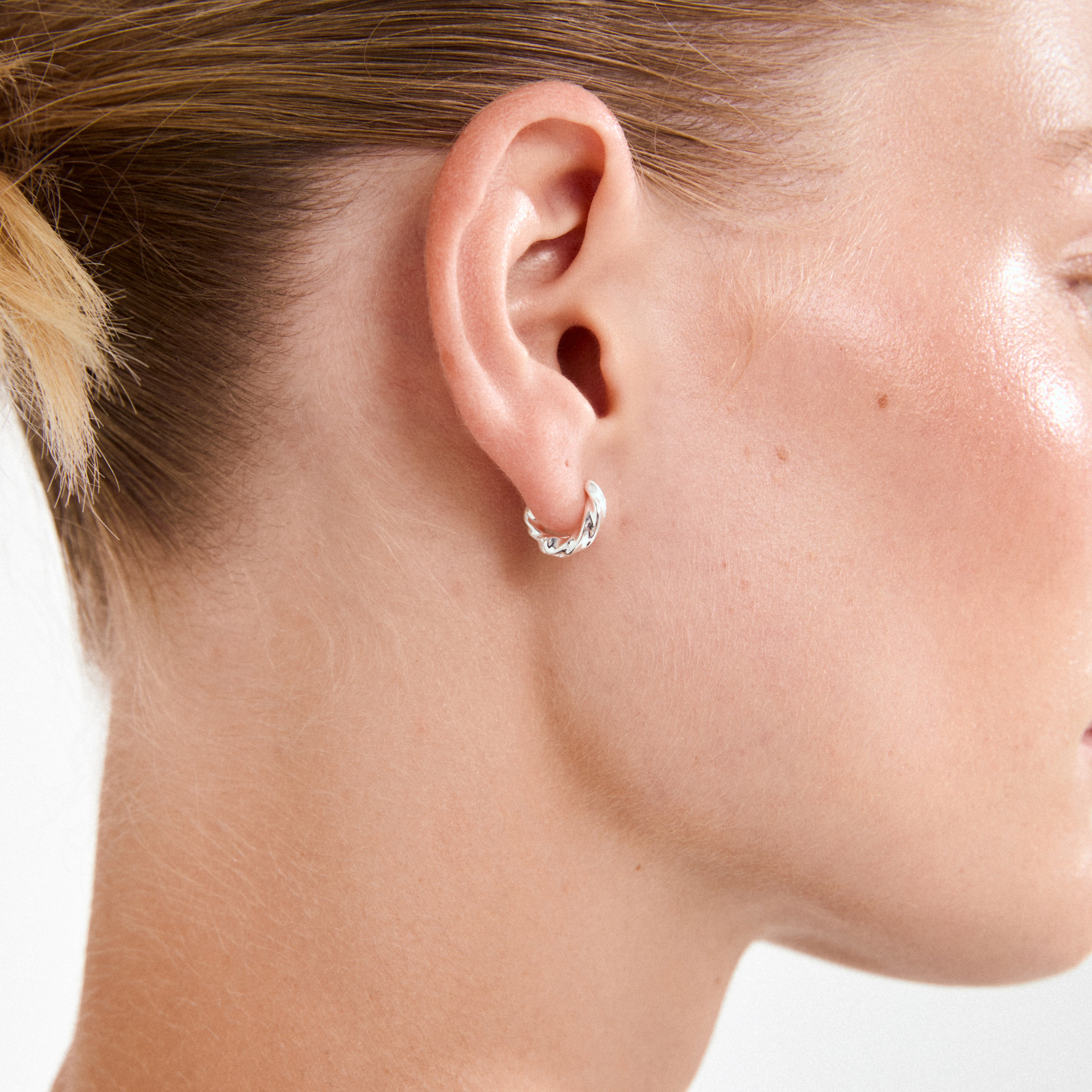 Close-up of a person's ear adorned with Pilgrim's TAFFY small swirl hoop earrings, silver-plated, capturing their wavy, nature-inspired design and handcrafted appeal.