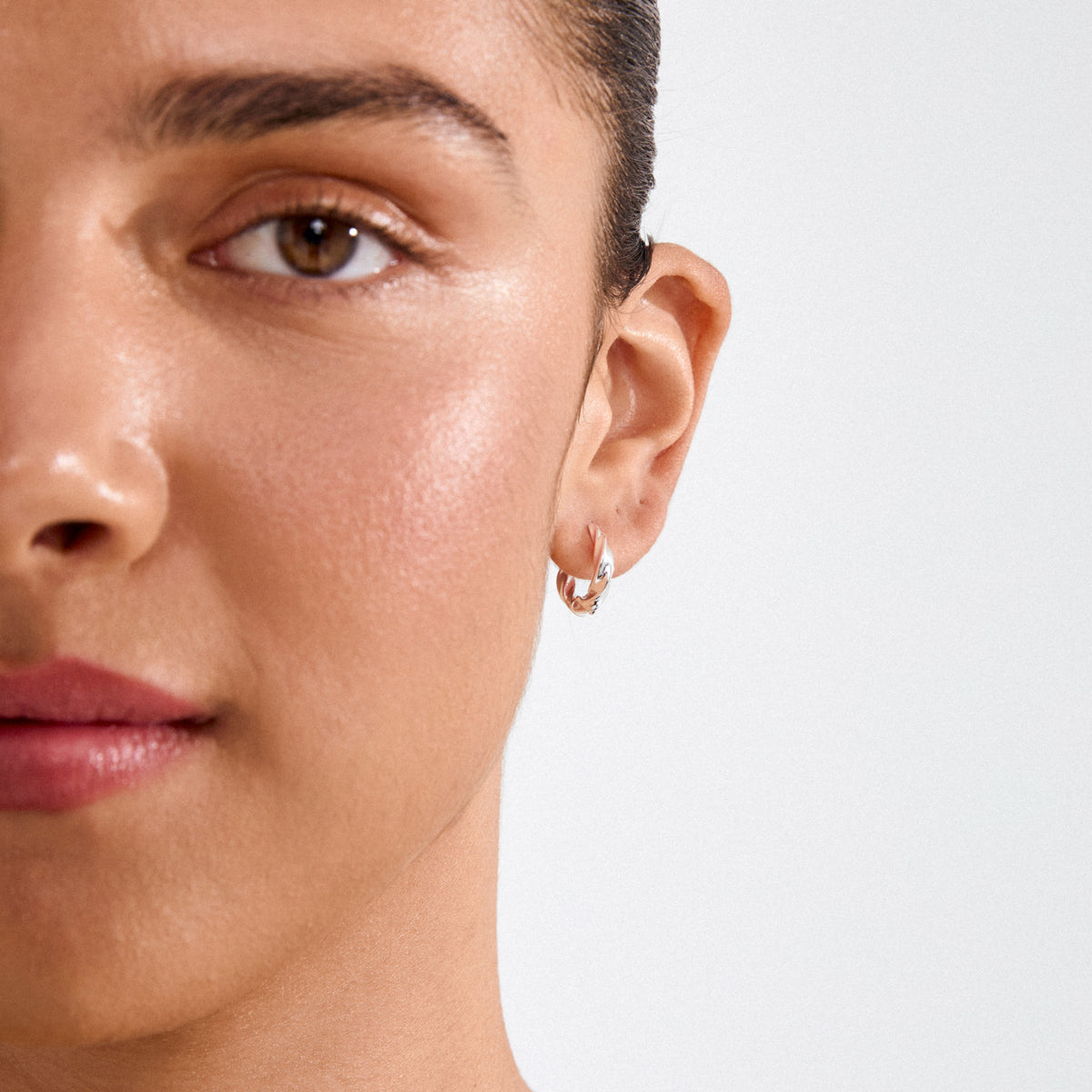 Close-up of a woman's face wearing Pilgrim's TAFFY medium-size swirl hoop earrings, silver-plated, showcasing their elegant twisted design and vintage-inspired curves.