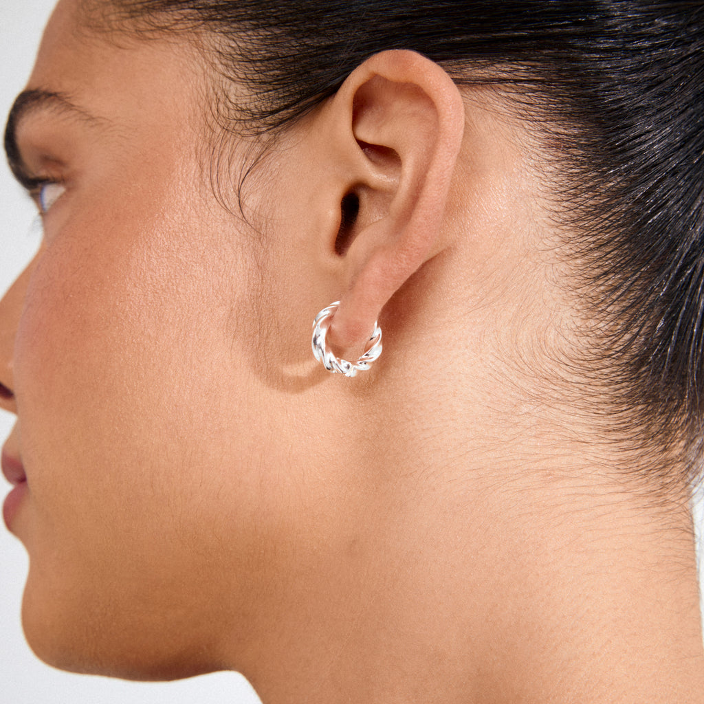 Close-up of a person's ear wearing Pilgrim's TAFFY medium silver-plated swirl hoop earring, showcasing its twisted-rope design and vintage-inspired elegance.