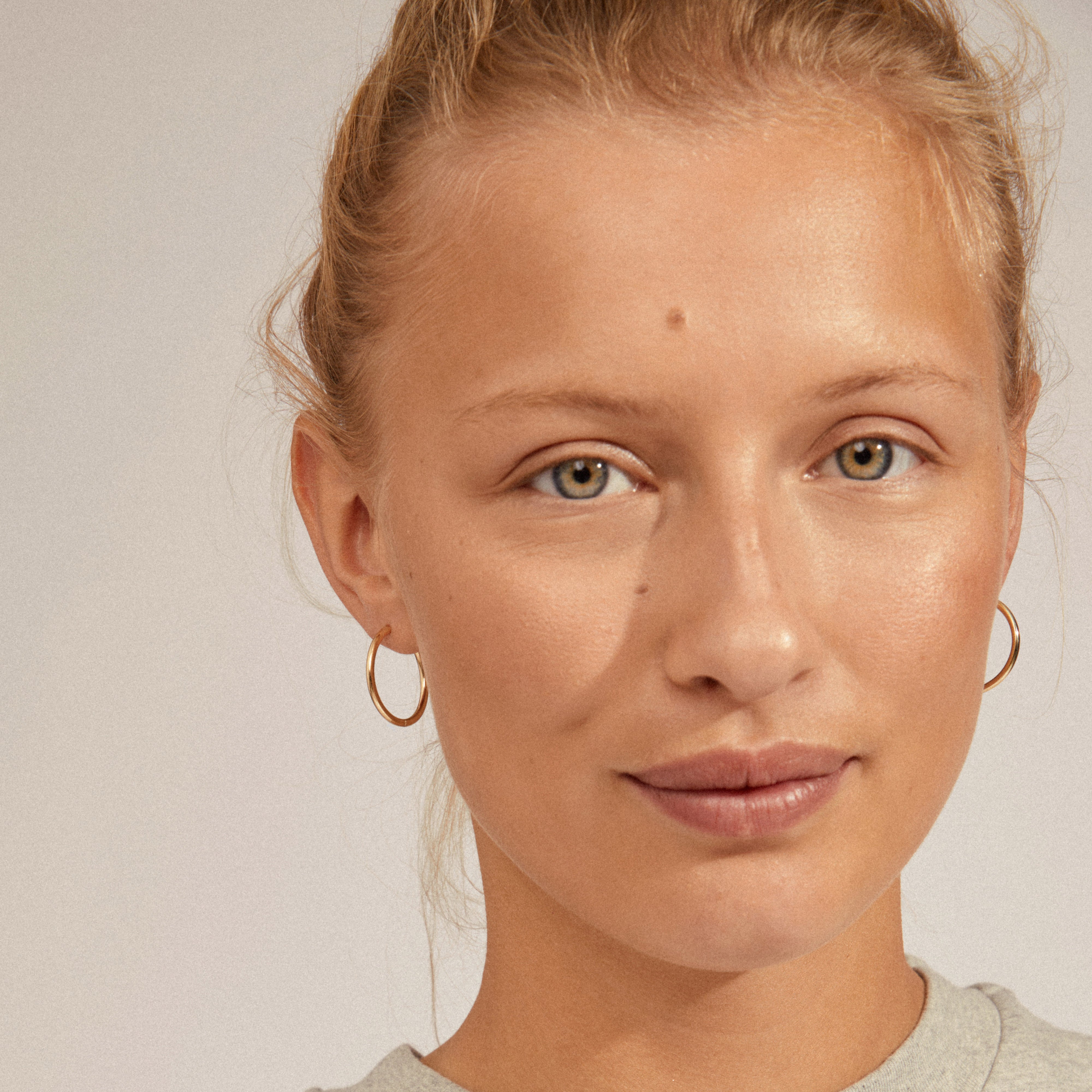 Woman wearing APRIL small, gold-plated hoop earrings by Pilgrim, showcasing their elegant design perfect for casual and special occasions.