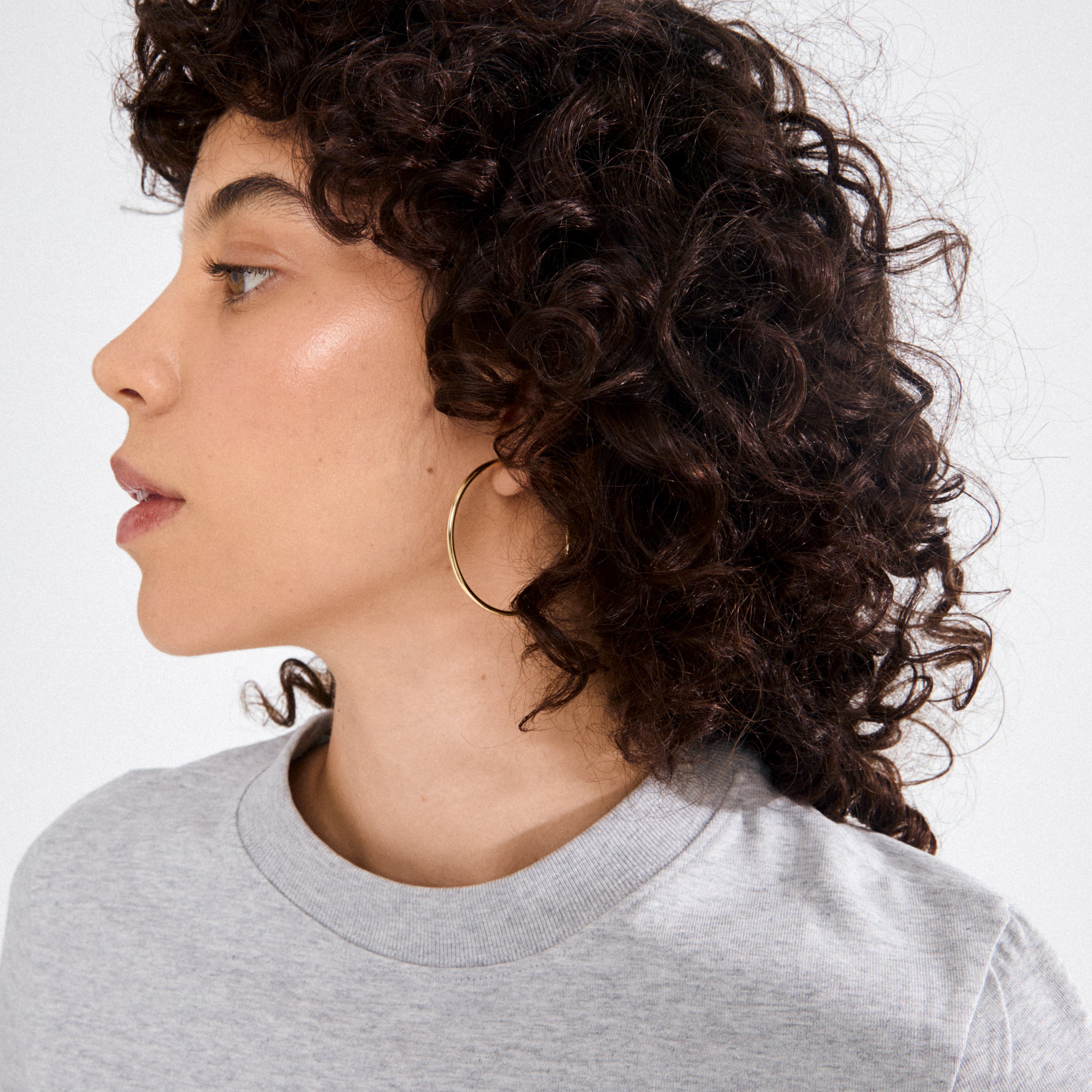 APRIL medium-size gold-plated hoop earring worn by a young woman, showcasing its 40 mm diameter and recycled craftsmanship in a clean studio setting.